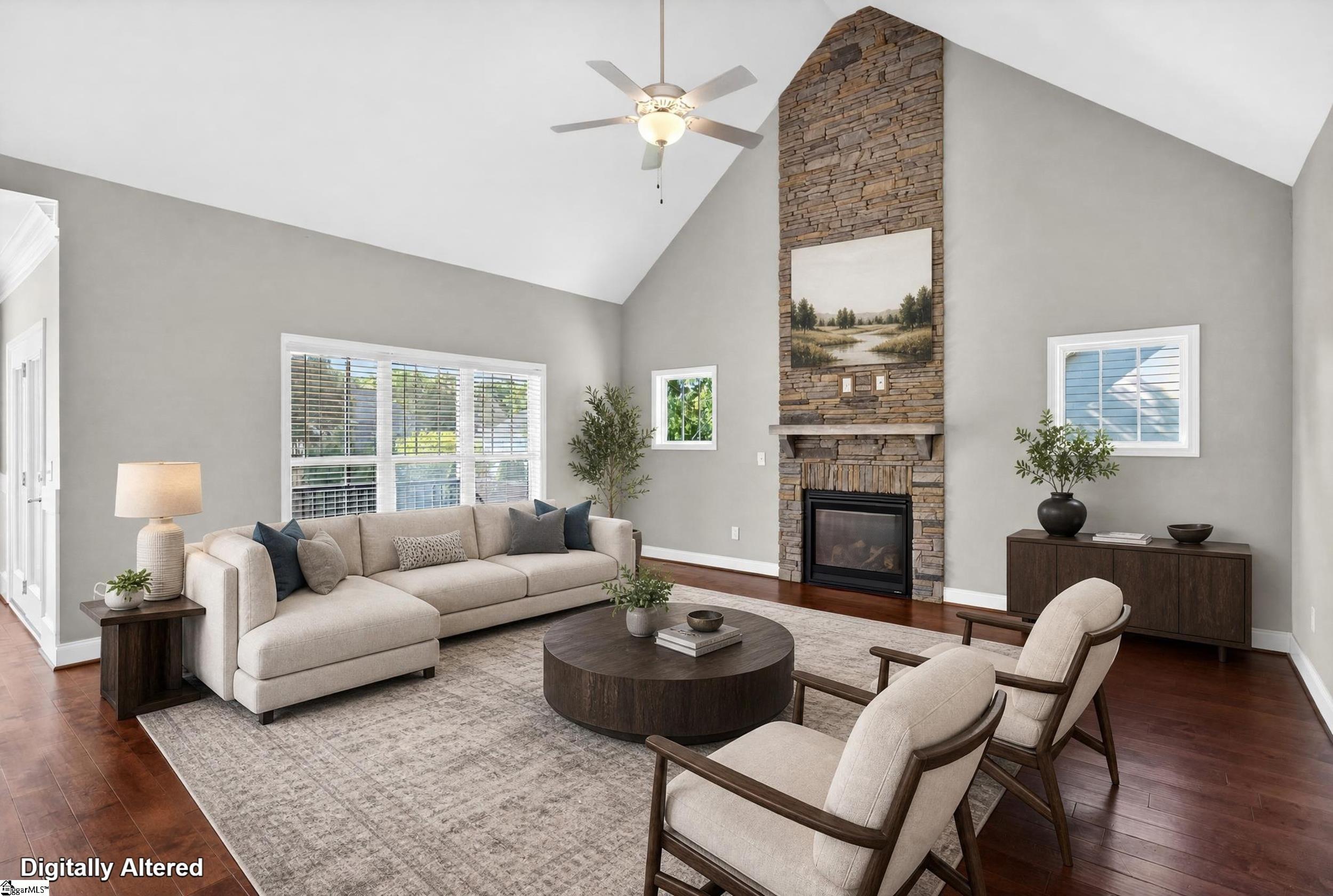 Staged living room with vaulted ceiling, tall stone fireplace, beige sectional, and two armchairs.