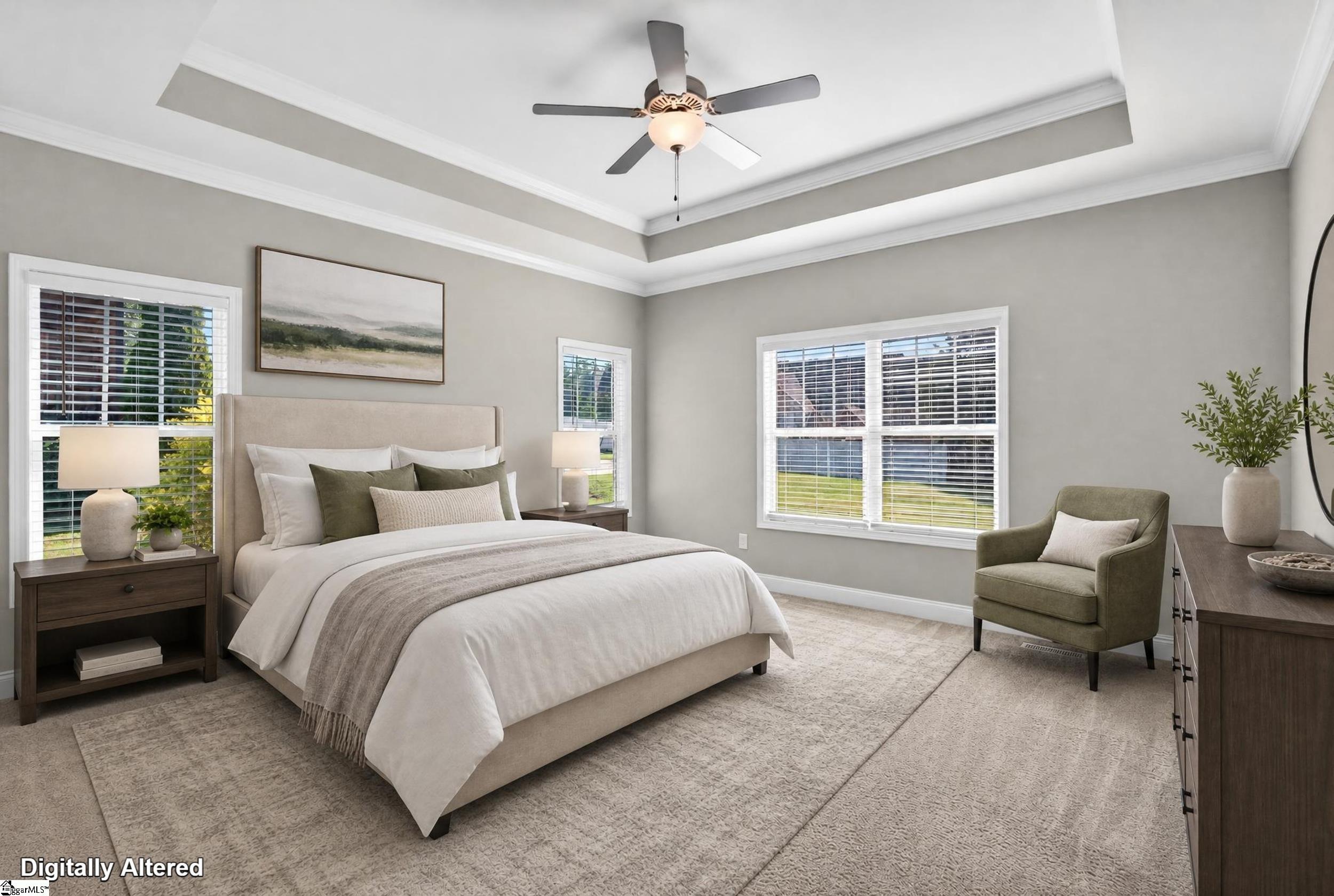 Staged bedroom with an upholstered bed, tray ceiling, ceiling fan, and windows with blinds.