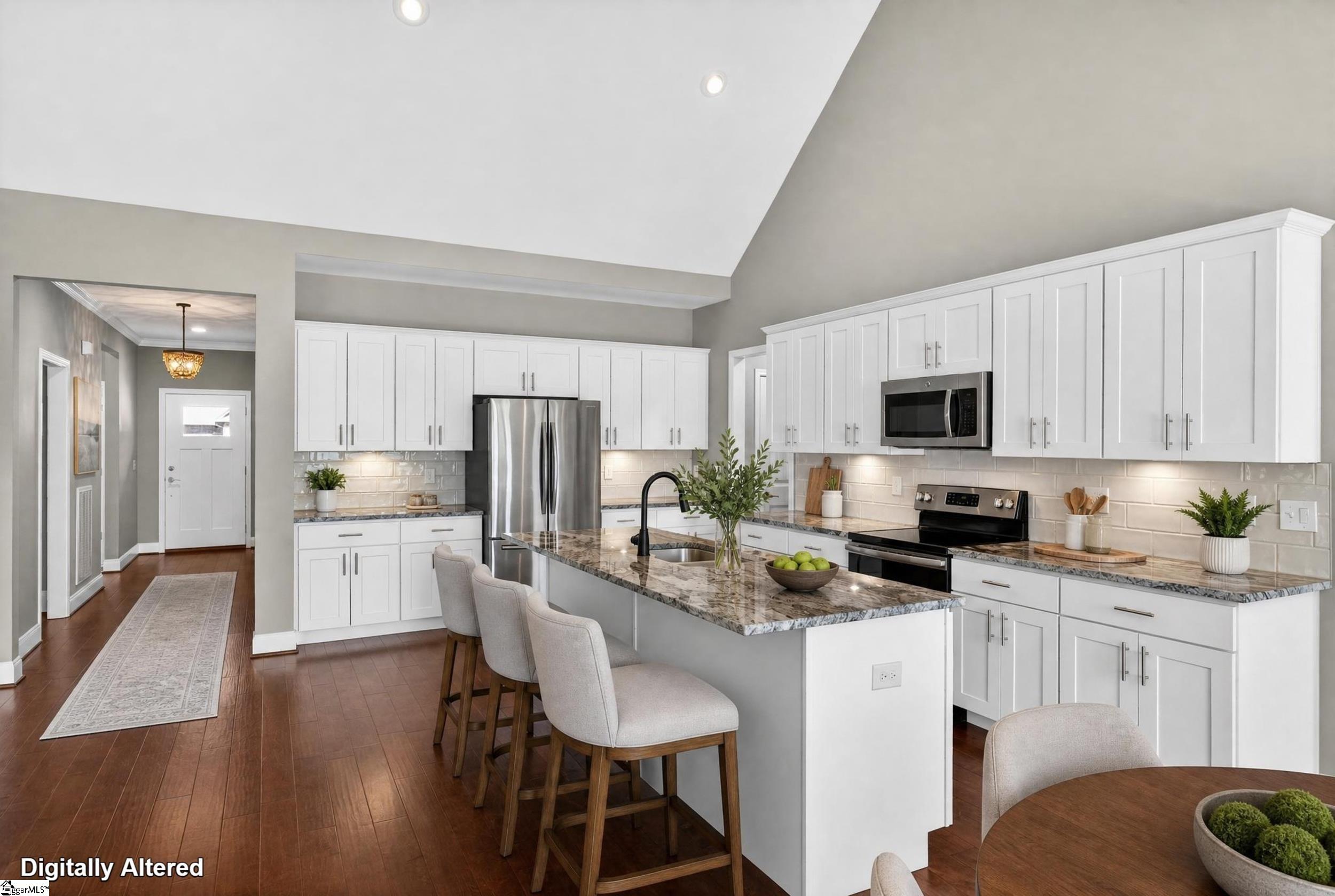 Kitchen with white cabinets, a marble-patterned island, stainless steel appliances, and a vaulted ceiling.