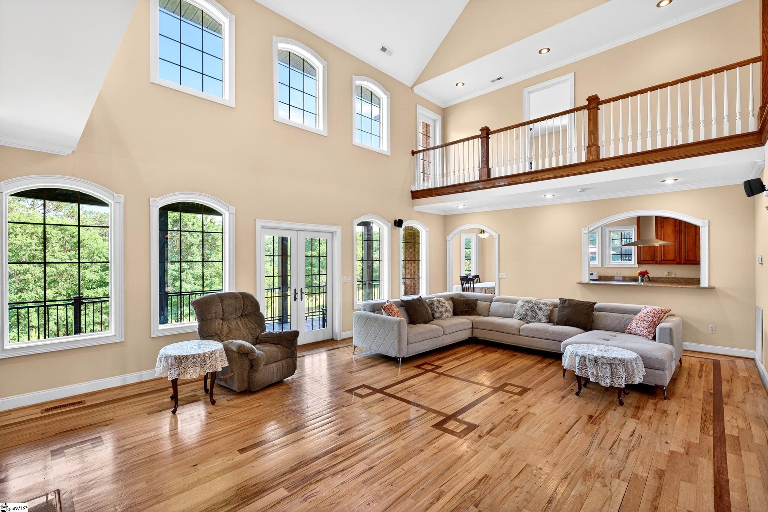 Living room with tall windows, hardwood floors, and an upstairs gallery railing.