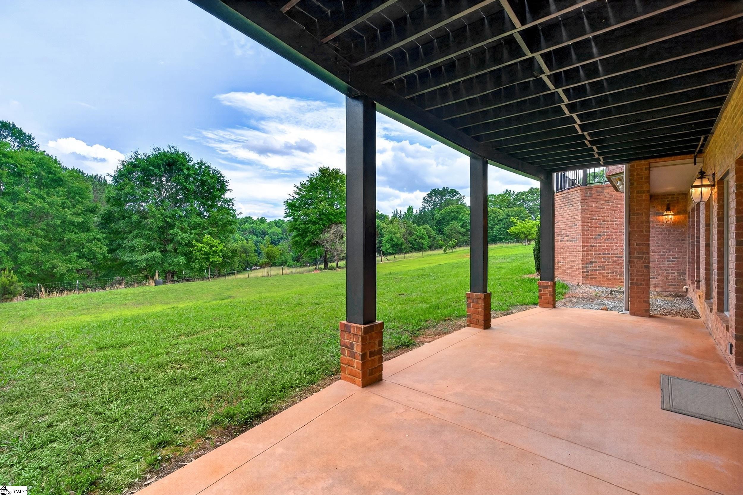 Covered patio with dark rafters overlooks a wide green lawn and mature trees.