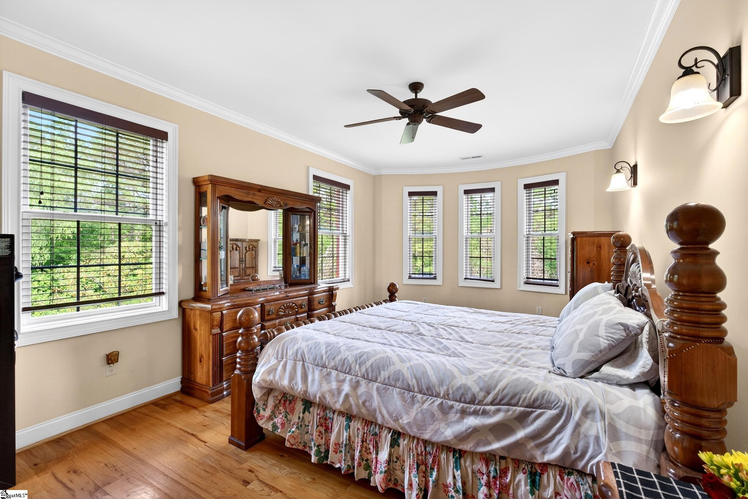 Bedroom with a carved wooden bed, matching dresser and mirror, and several windows.