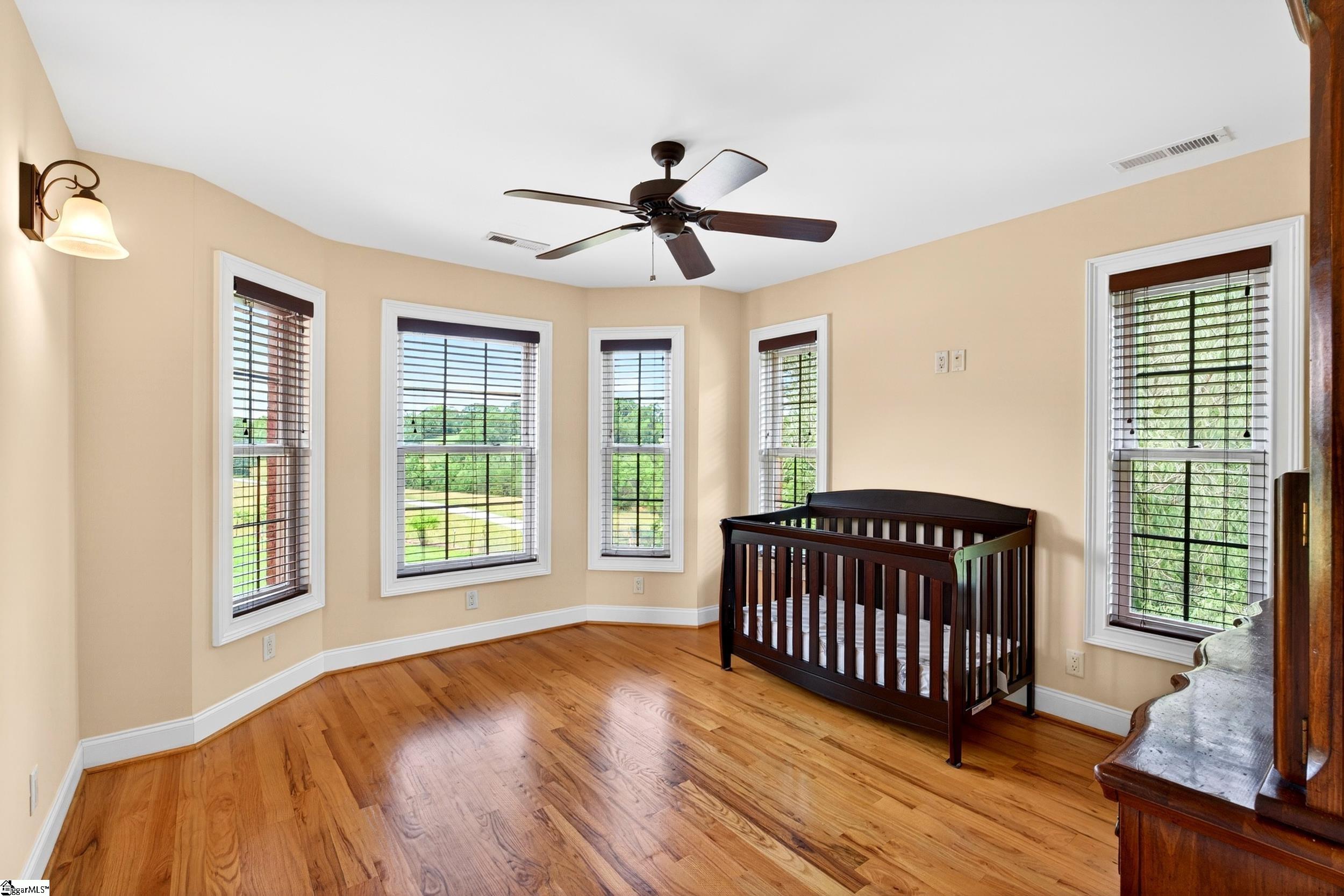 Nursery with a dark wooden crib, hardwood floors, and multiple windows.