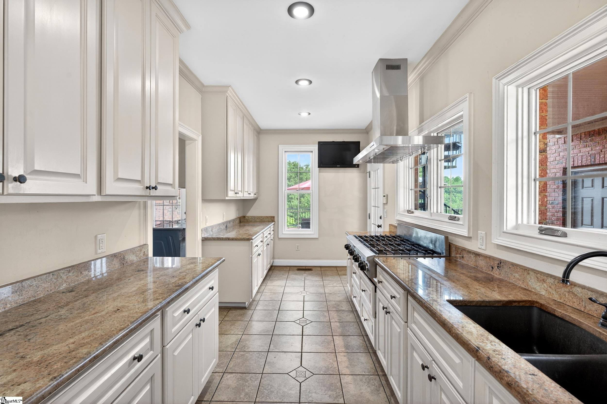 Kitchen with white cabinets, granite counters, a gas range, and large windows.