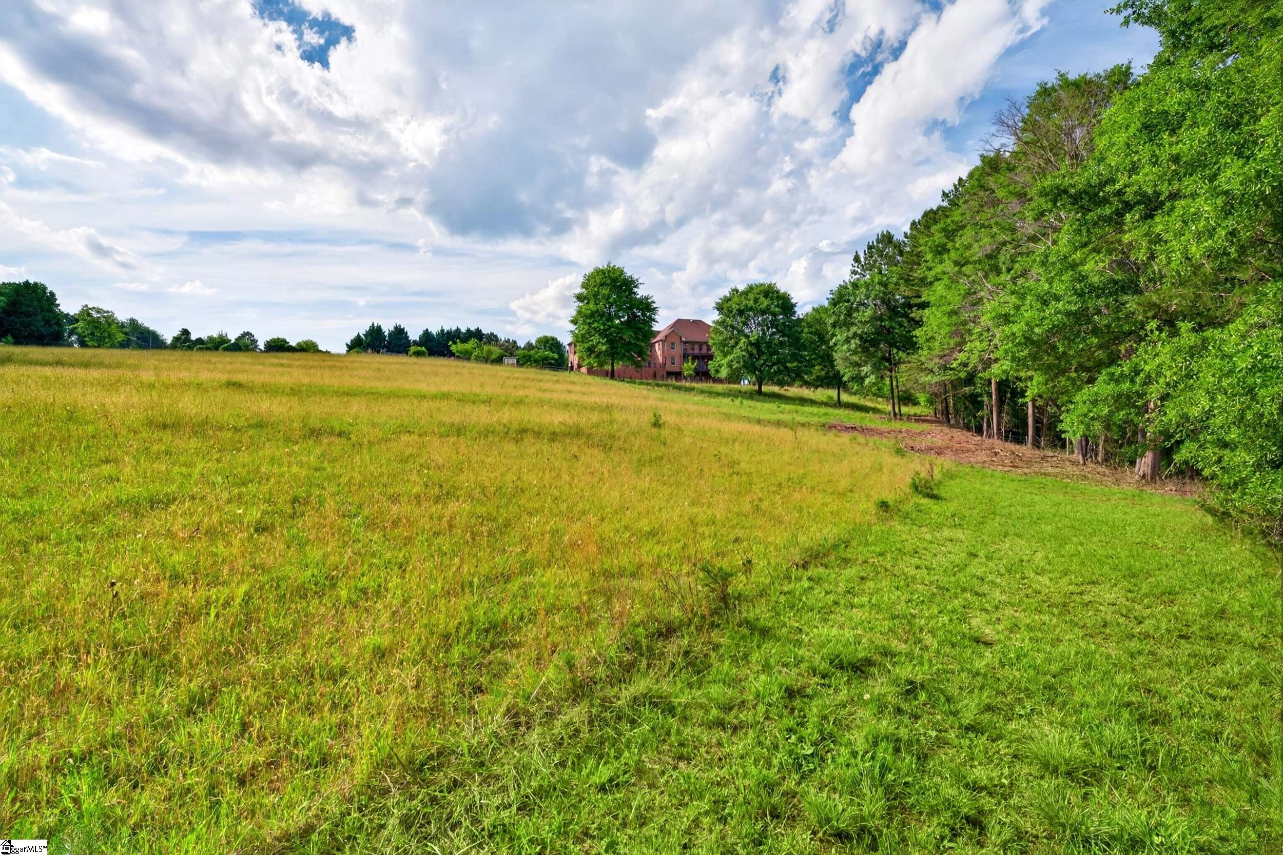 Brick house beyond a wide grassy field bordered by mature trees.