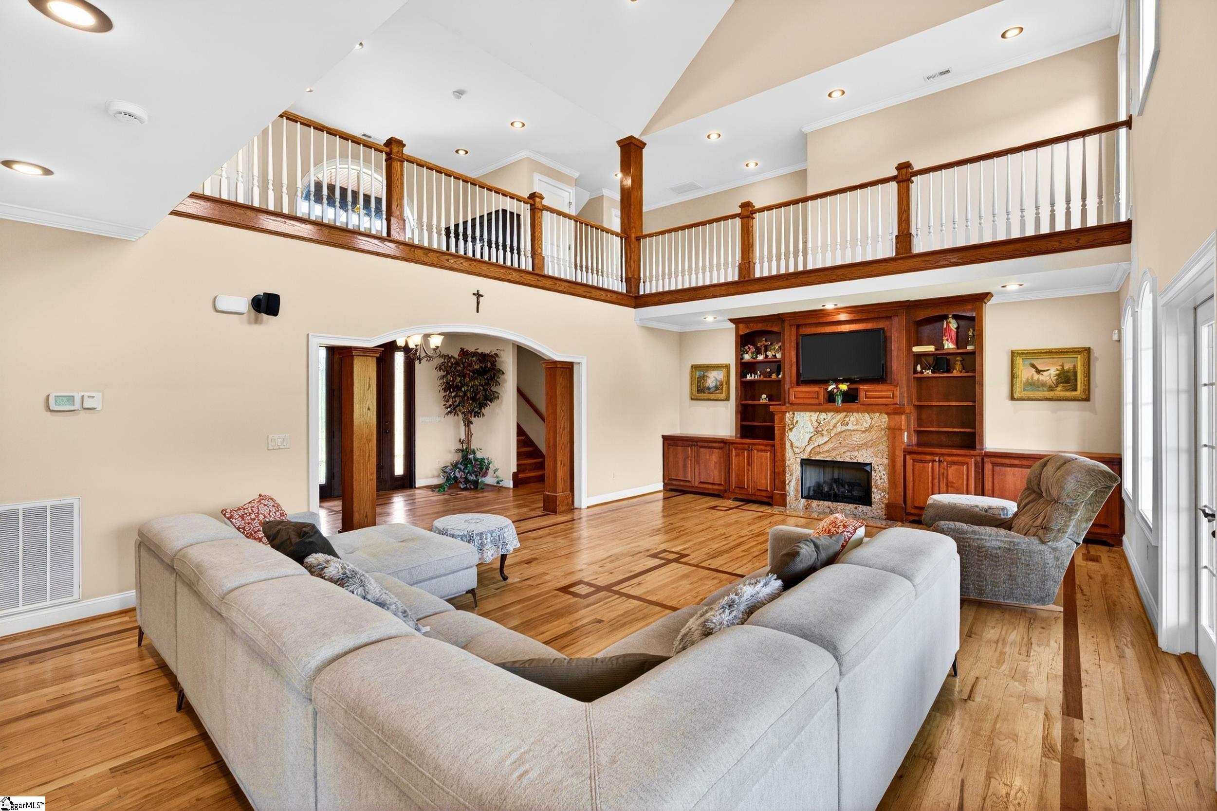 Living room with a stone fireplace, built-in wood cabinetry, hardwood floors, and an open upper-level balcony.
