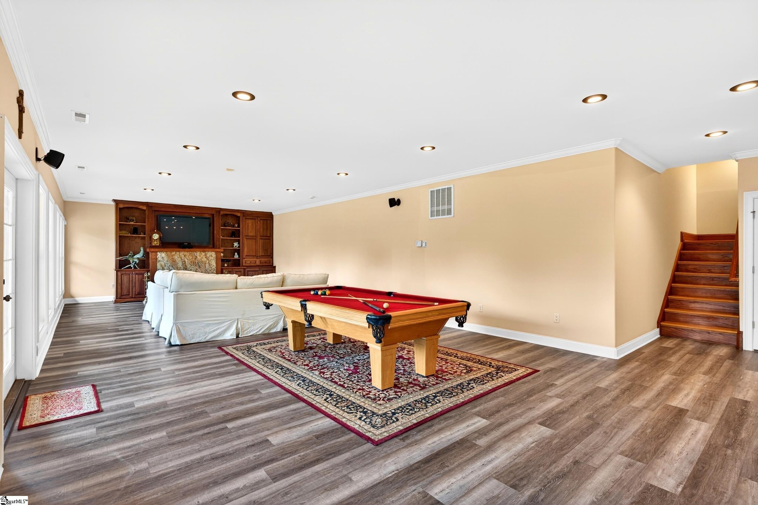 Basement game room with a red-felt pool table, built-in entertainment center, and wooden staircase.
