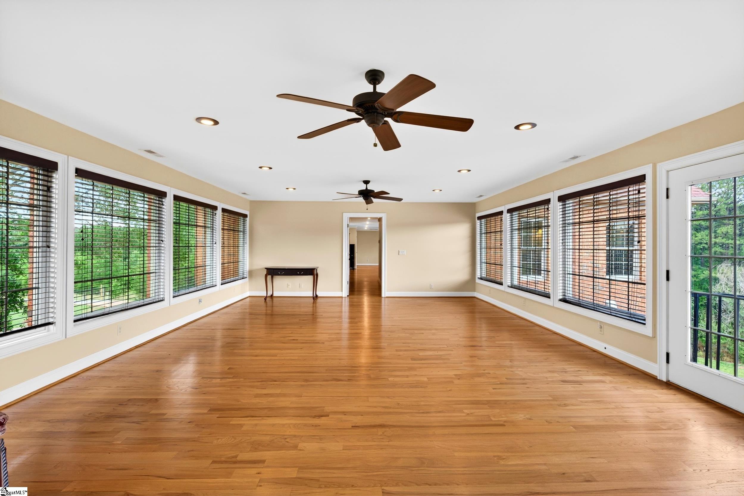 Spacious living room with hardwood floors, large windows, and two ceiling fans.