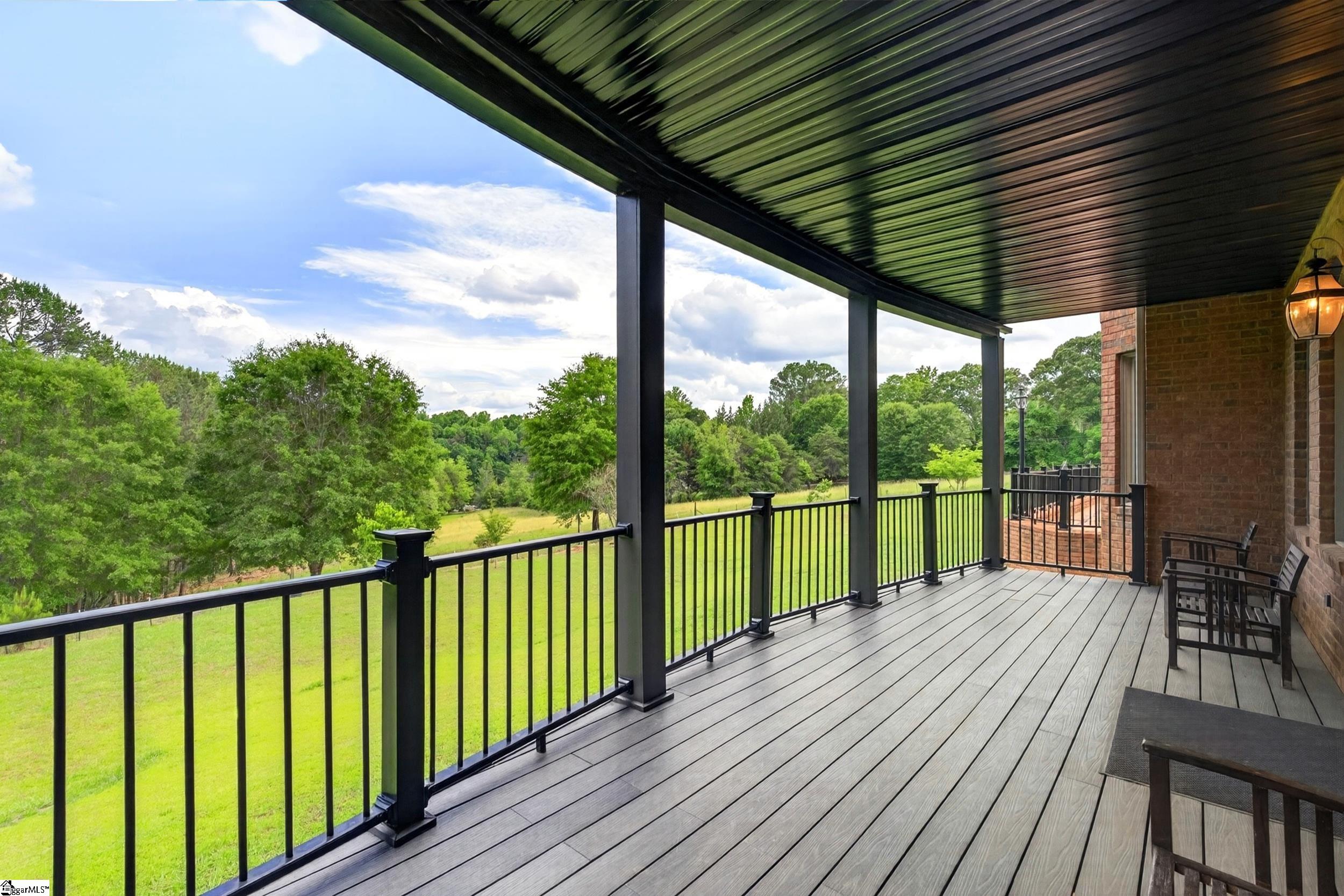 Covered deck with black railings and seating overlooking a green lawn and mature trees.