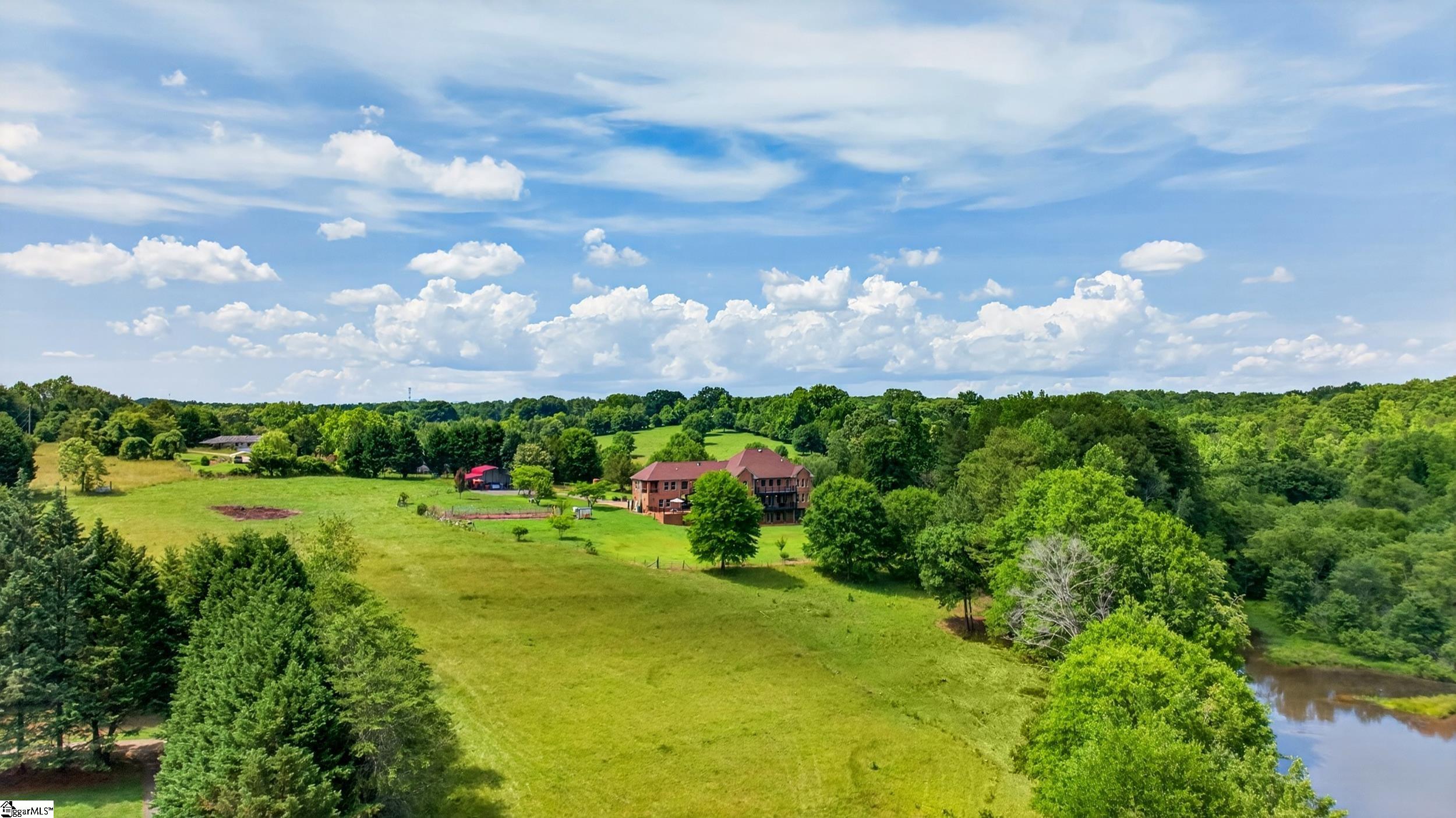 Aerial view of a brick home surrounded by broad green pasture, trees, and a pond.