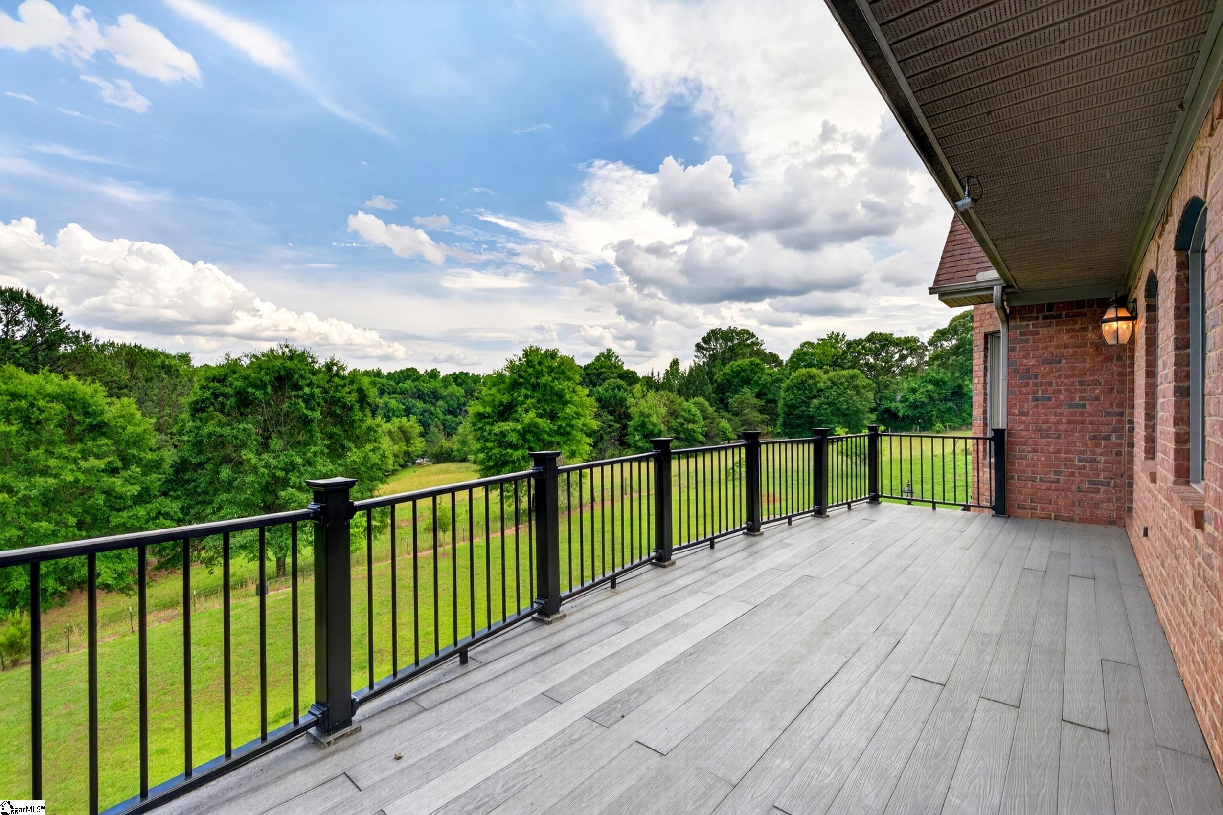Wide deck with black railings overlooking a green lawn and wooded landscape.