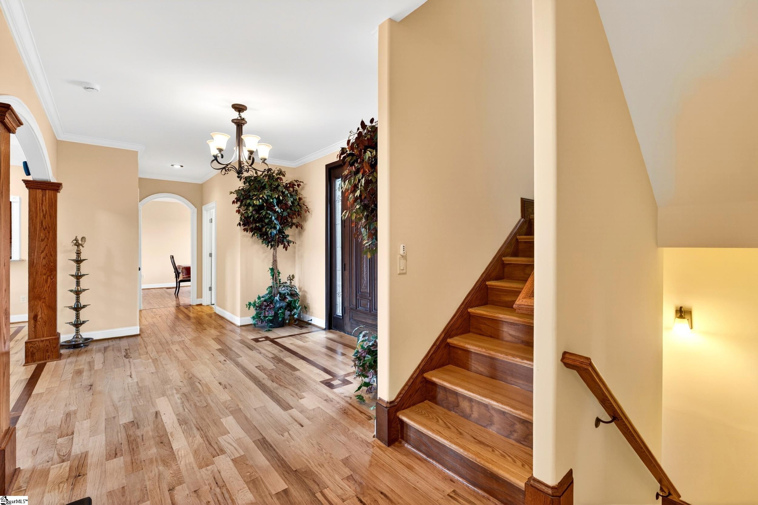 Foyer with wood floors and a dark wood staircase beside an arched entryway.