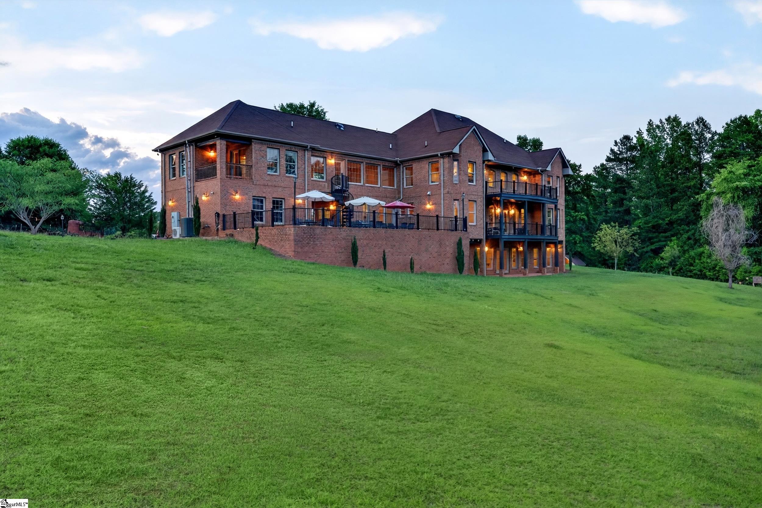 Two-story brick home with raised patio and balconies overlooking a sloping lawn at dusk.