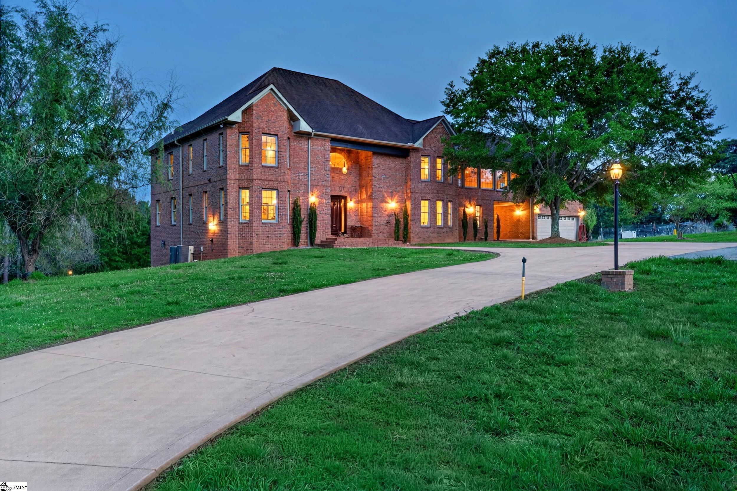 Two-story brick home with glowing windows and a broad curved driveway at dusk.