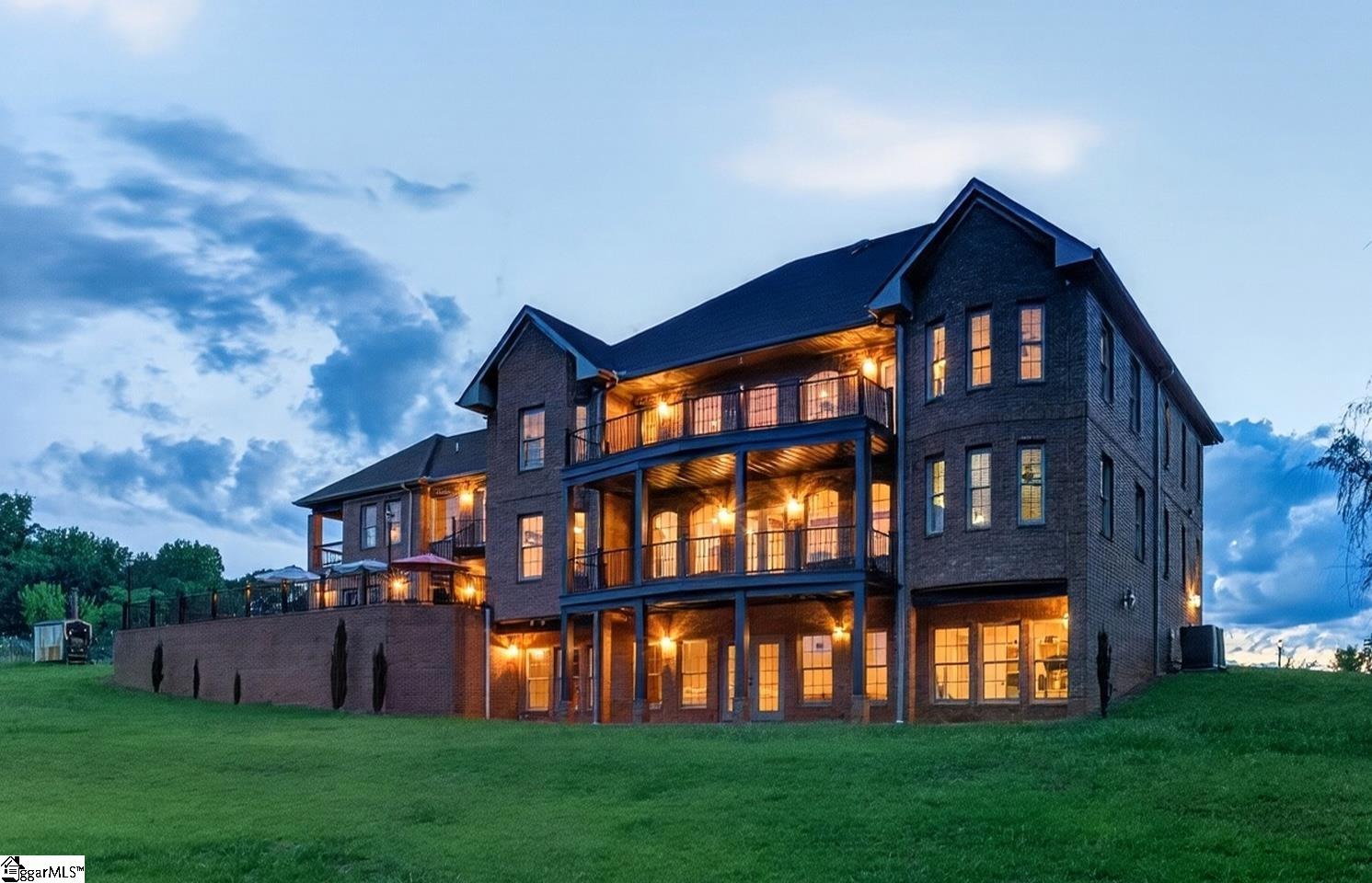 Large brick home with glowing windows and covered balconies at dusk.