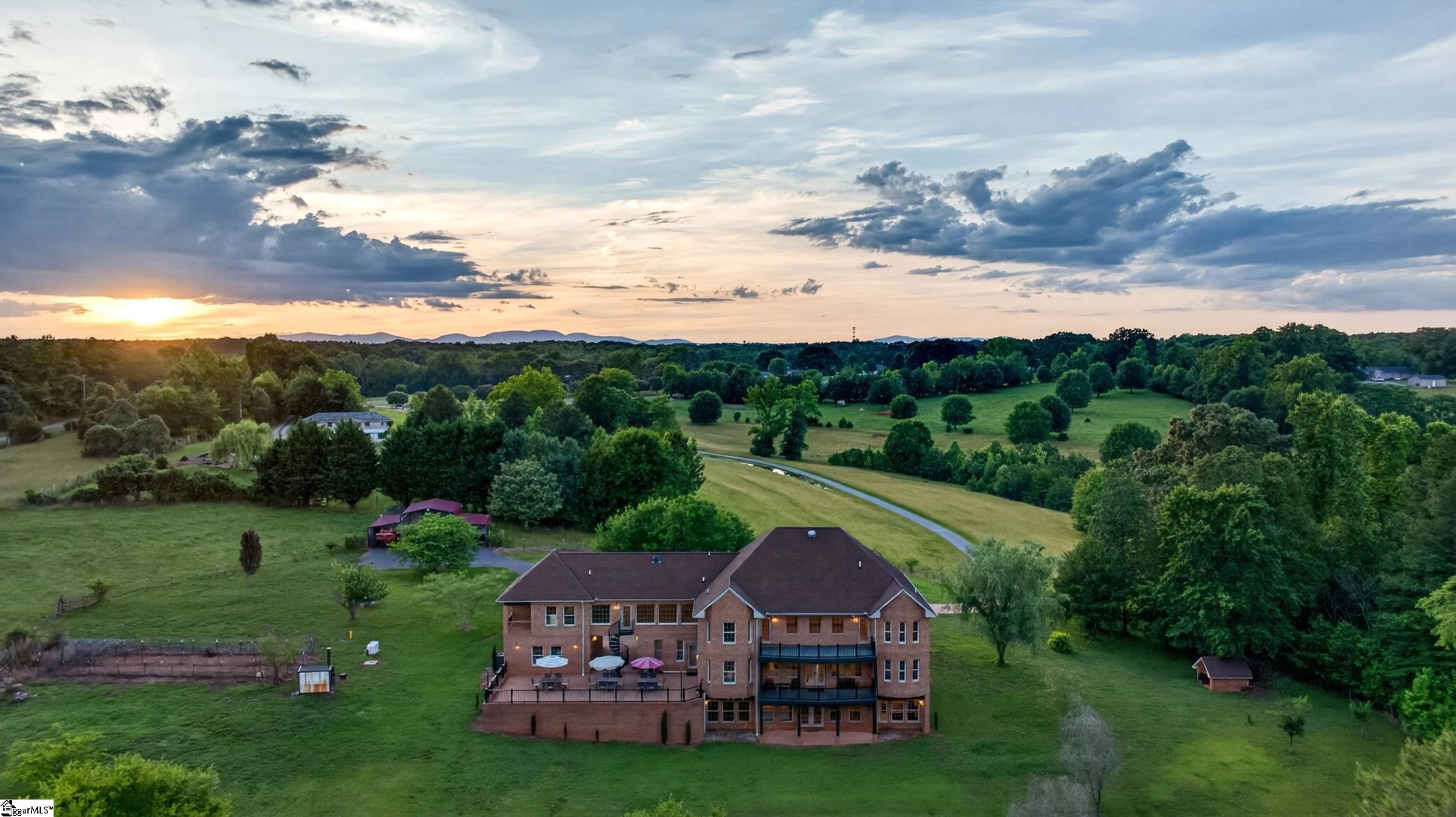 Large brick home with expansive lawns and wooded grounds at sunset, viewed from above.