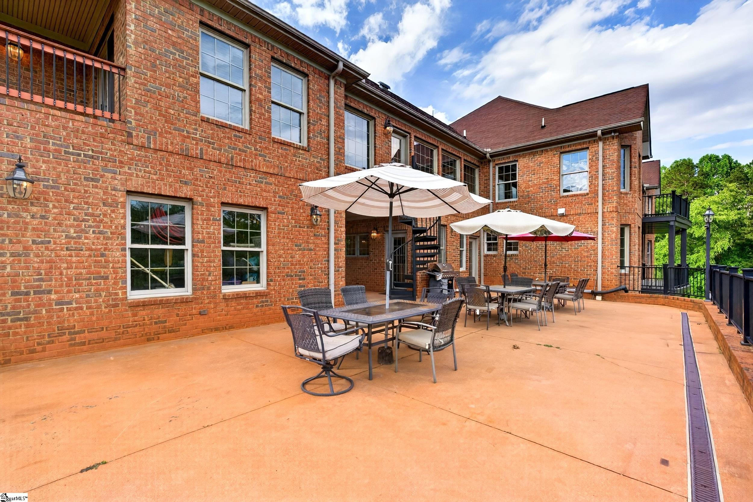 Brick home’s spacious patio with umbrella-shaded dining areas, black metal stairs, and upper balcony.