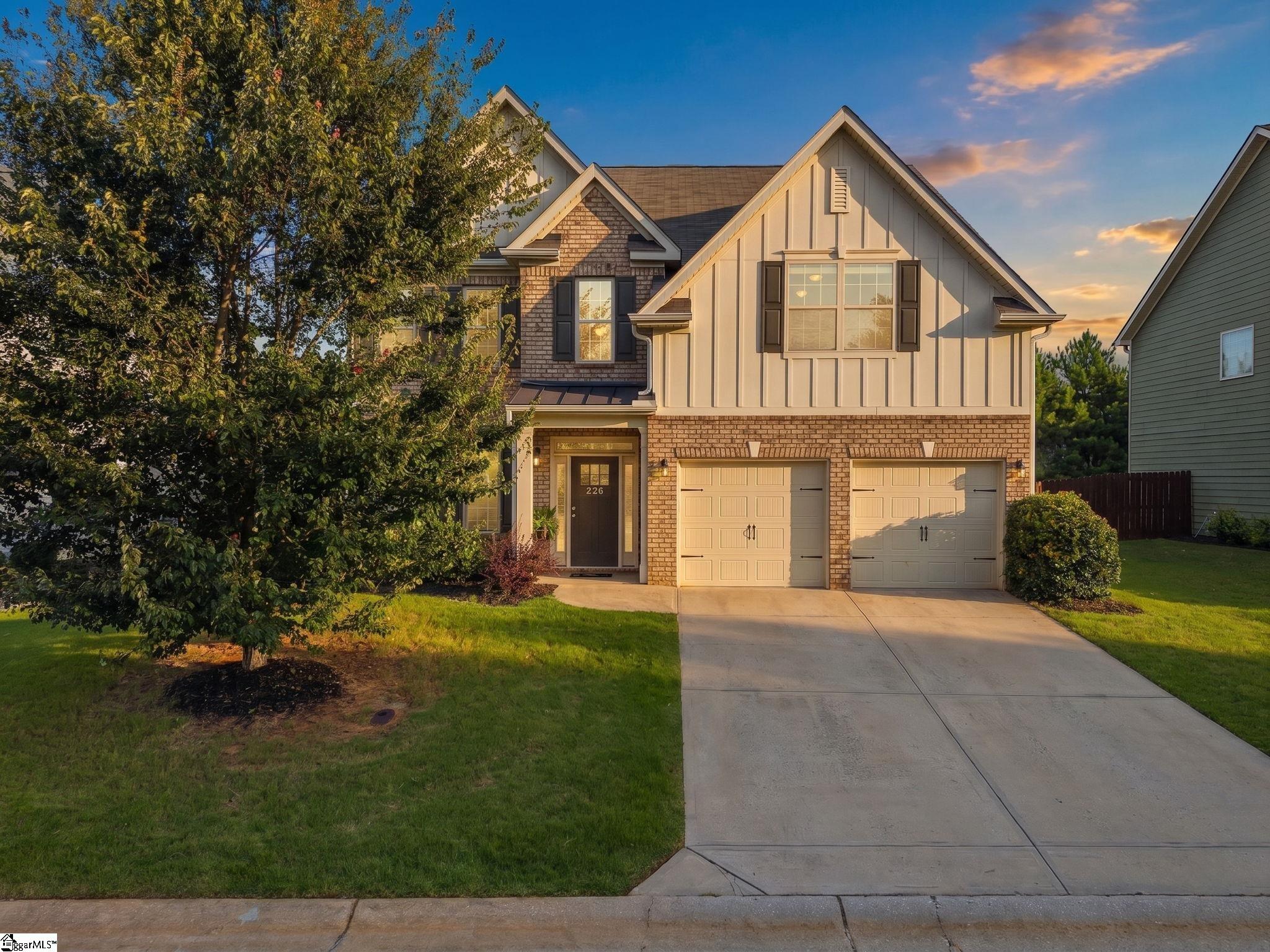 Two-story brick and siding home with two garage doors and a broad driveway at golden hour.