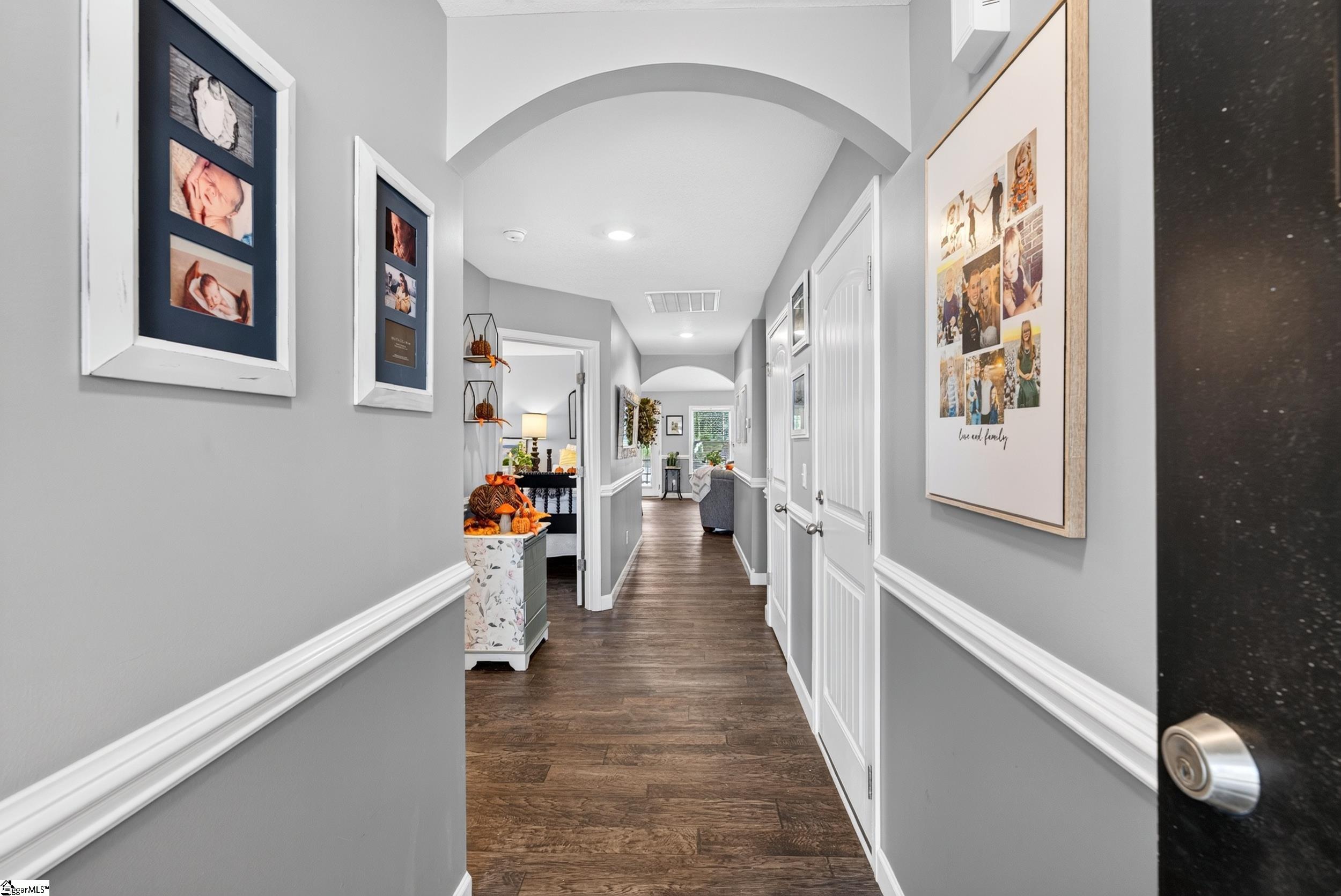 Furnished hallway with arched ceiling, dark wood floors, and family photo collages.