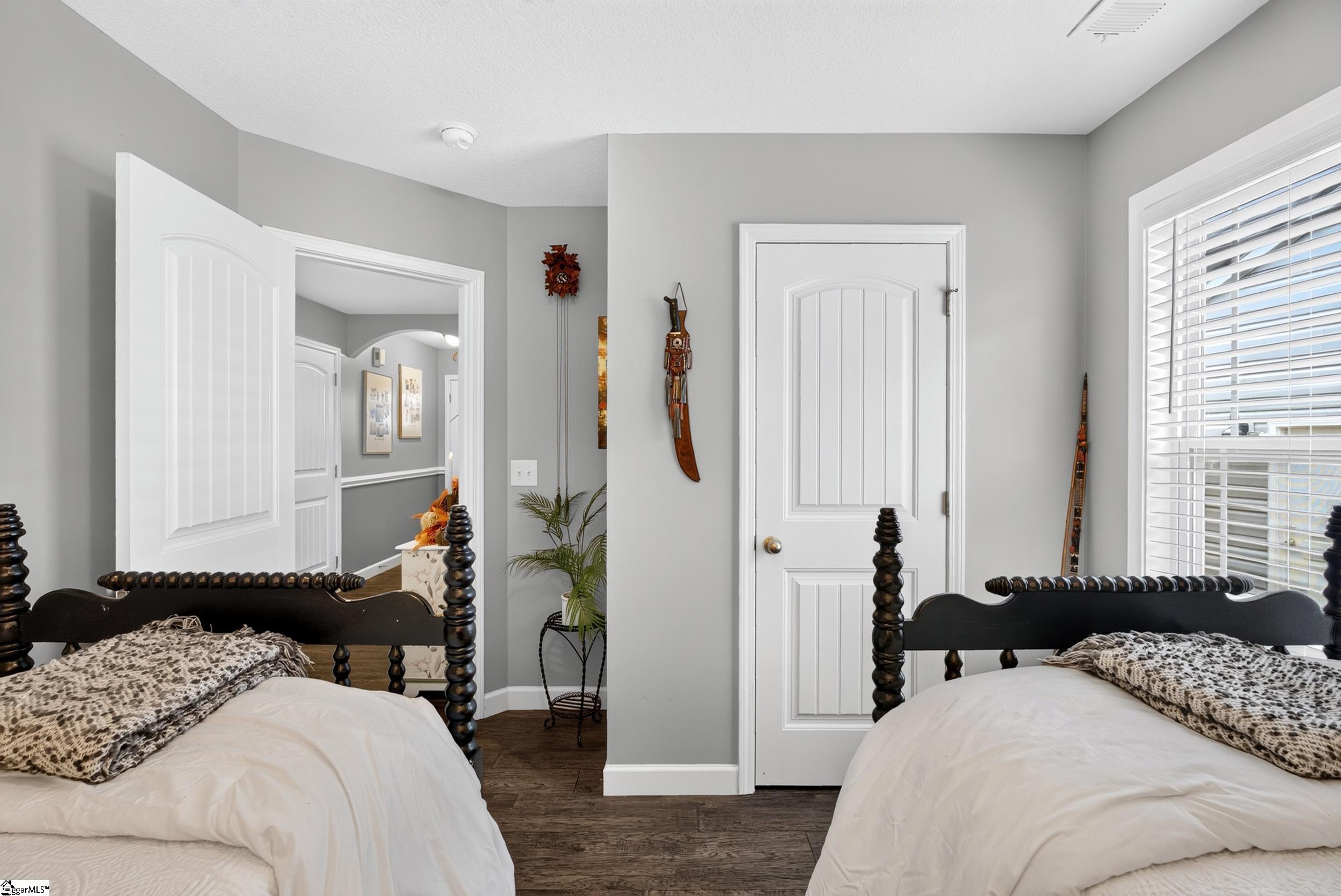 Bedroom with two white beds, dark carved frames, gray walls, and a window with white blinds.
