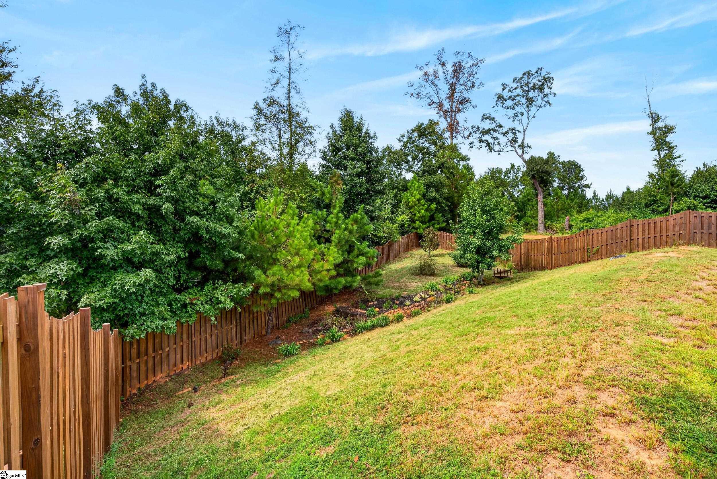 Sloped backyard with a wooden fence, landscaped beds, and a wooded edge.