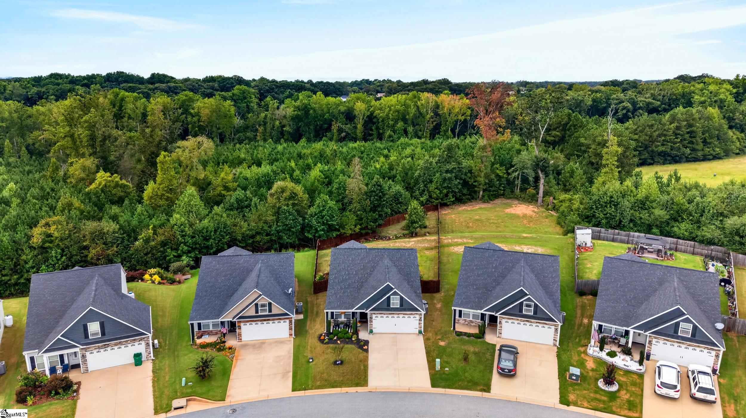 Aerial view of detached homes along a curved street, with fenced backyards and woods behind them.