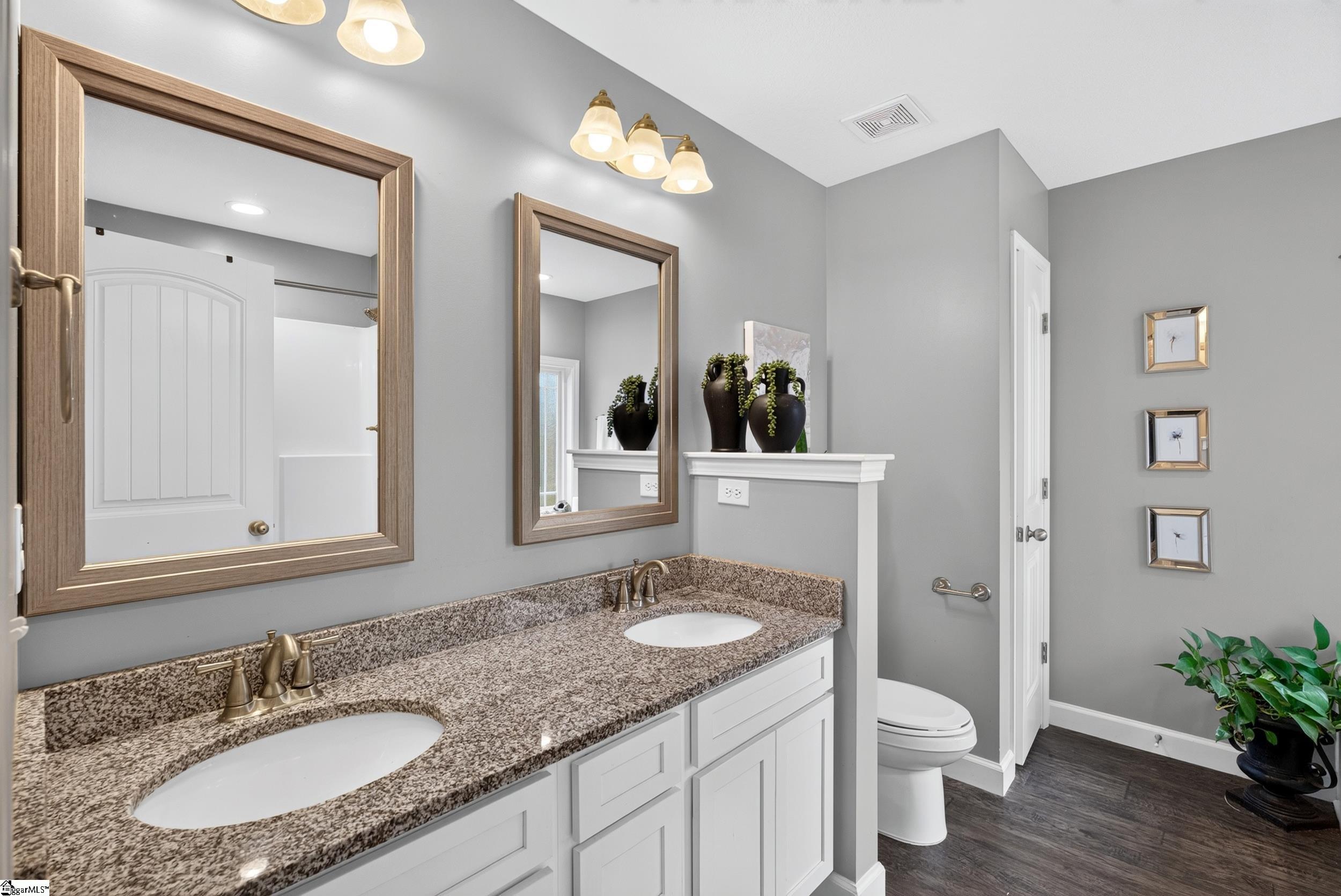 Bathroom with a double granite vanity, framed mirrors, and a toilet.