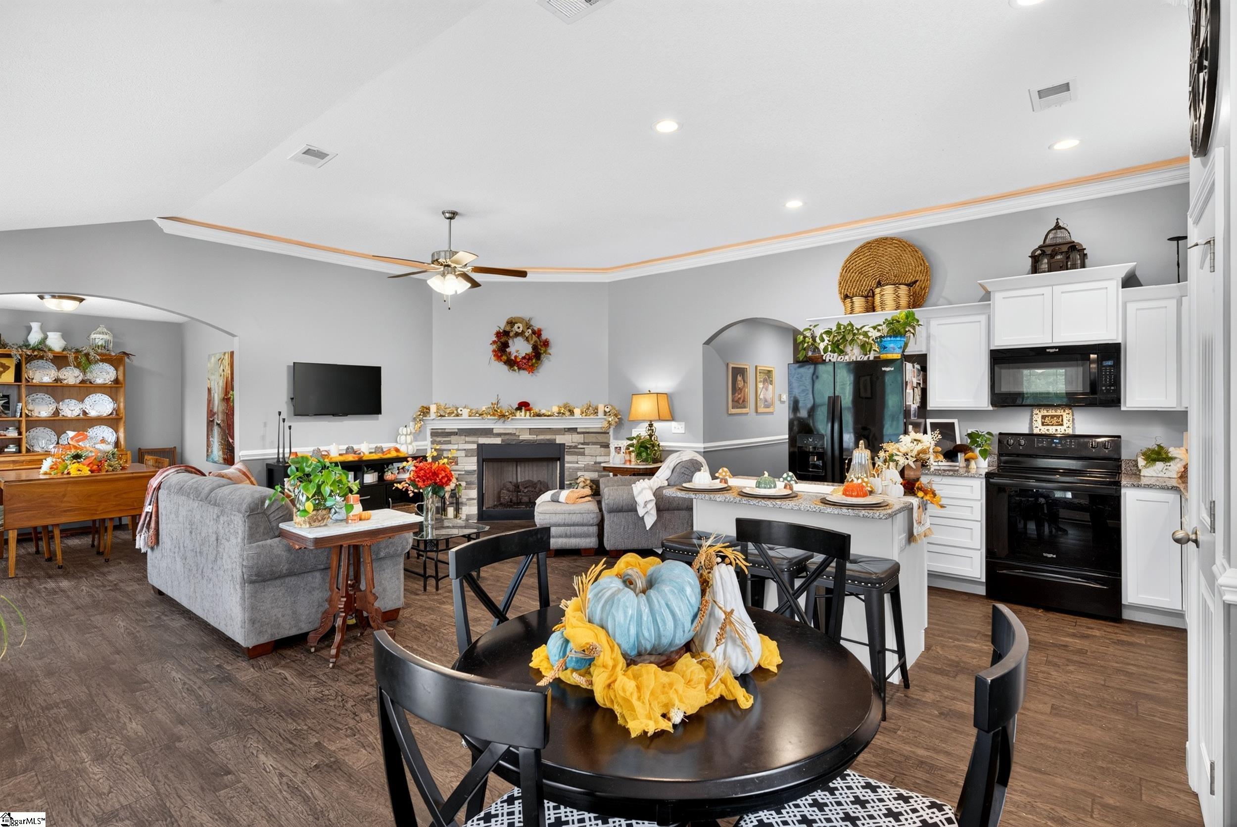 Open-plan kitchen and living room with a stone fireplace, white cabinetry, and a decorated dining table.