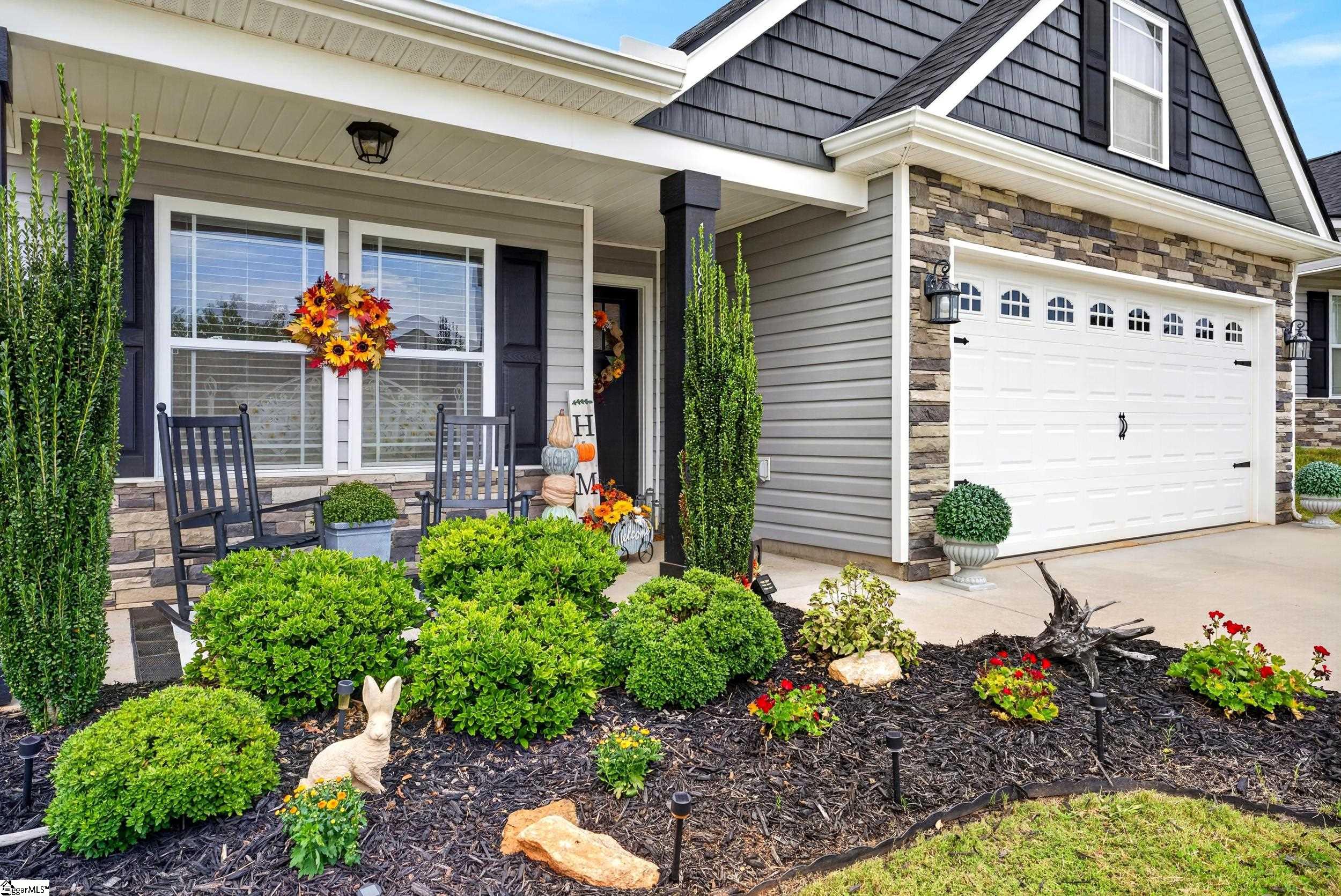 House exterior with a stone-faced garage, covered porch, rocking chairs, and autumn-decorated garden.
