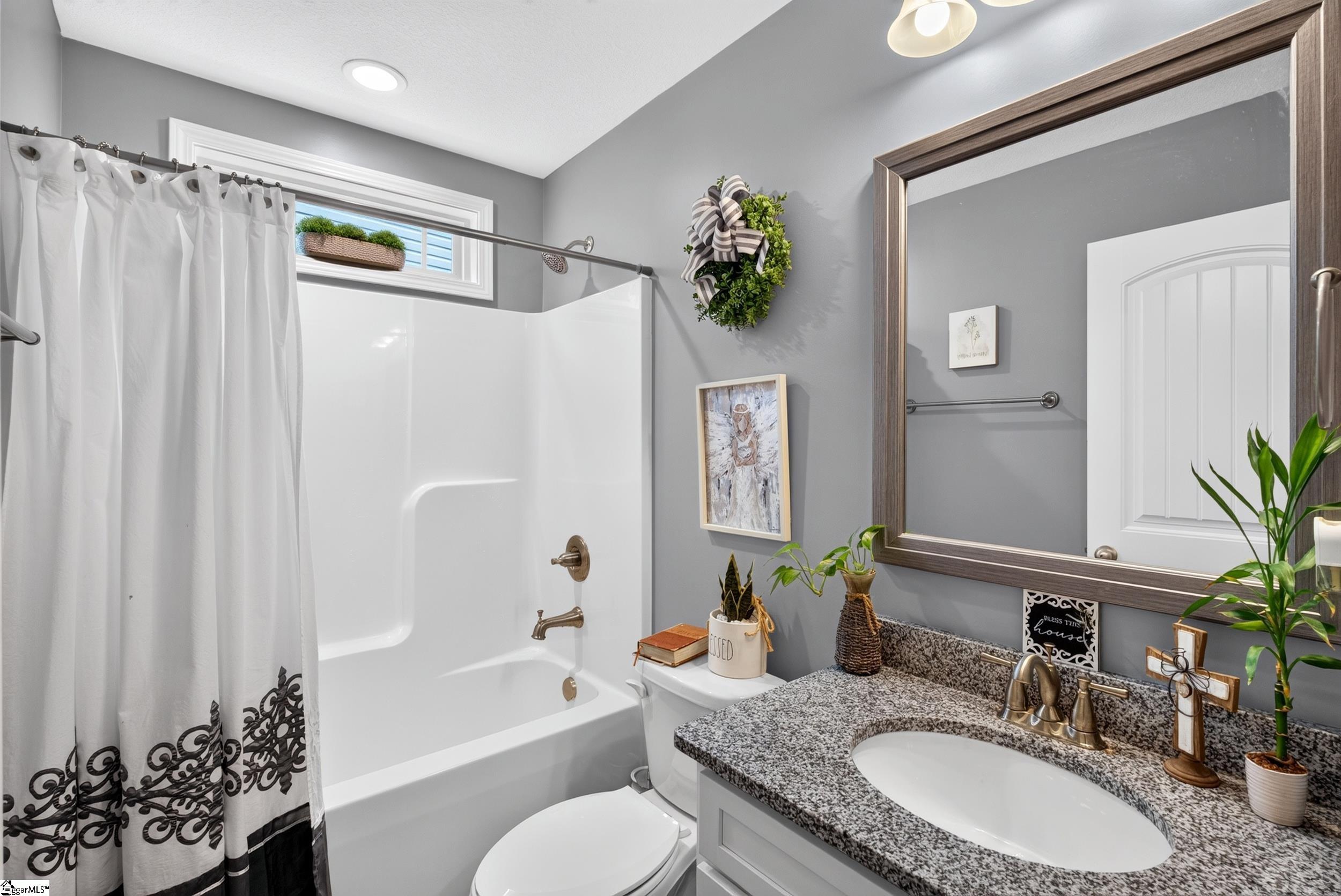 Bathroom with a white tub and shower, granite vanity, and large framed mirror.