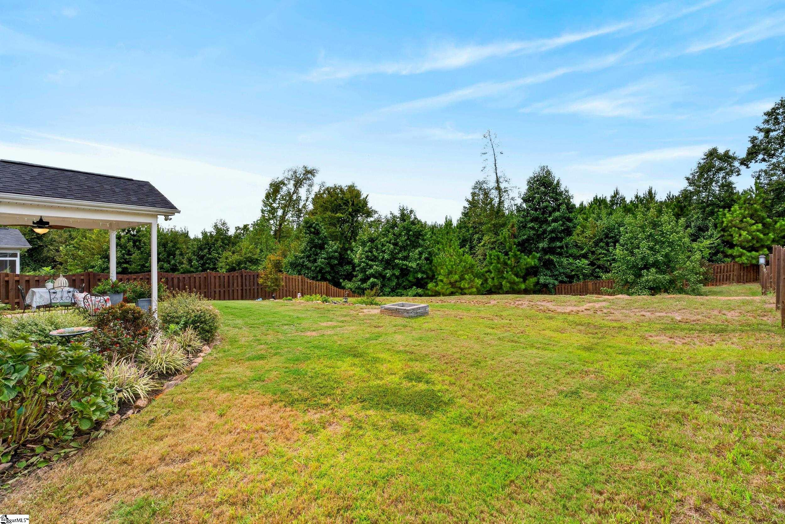 Backyard with a covered patio, fenced lawn, and square fire pit.