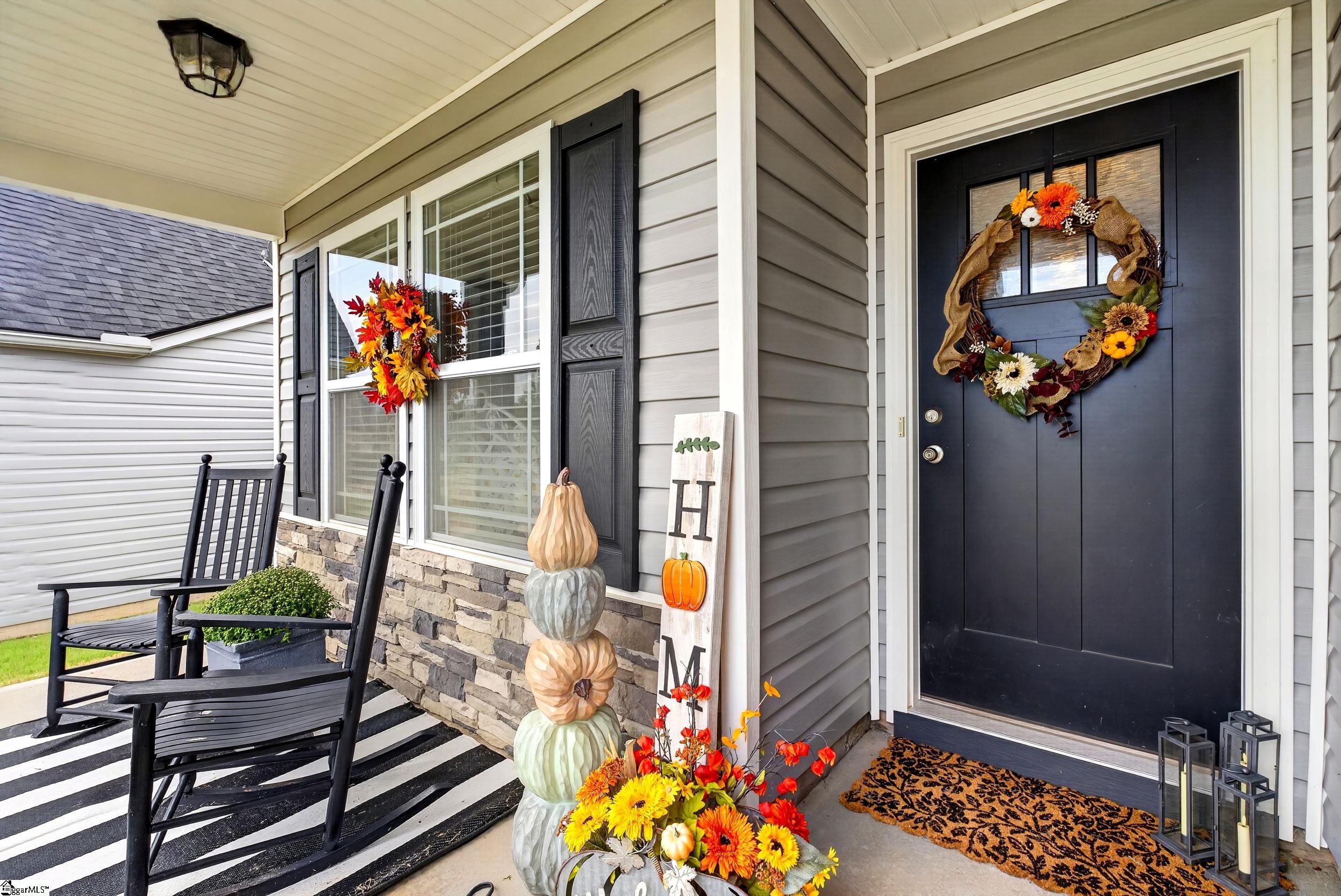 Home front porch with a black door, fall wreath, rocking chairs, and pumpkin decorations.