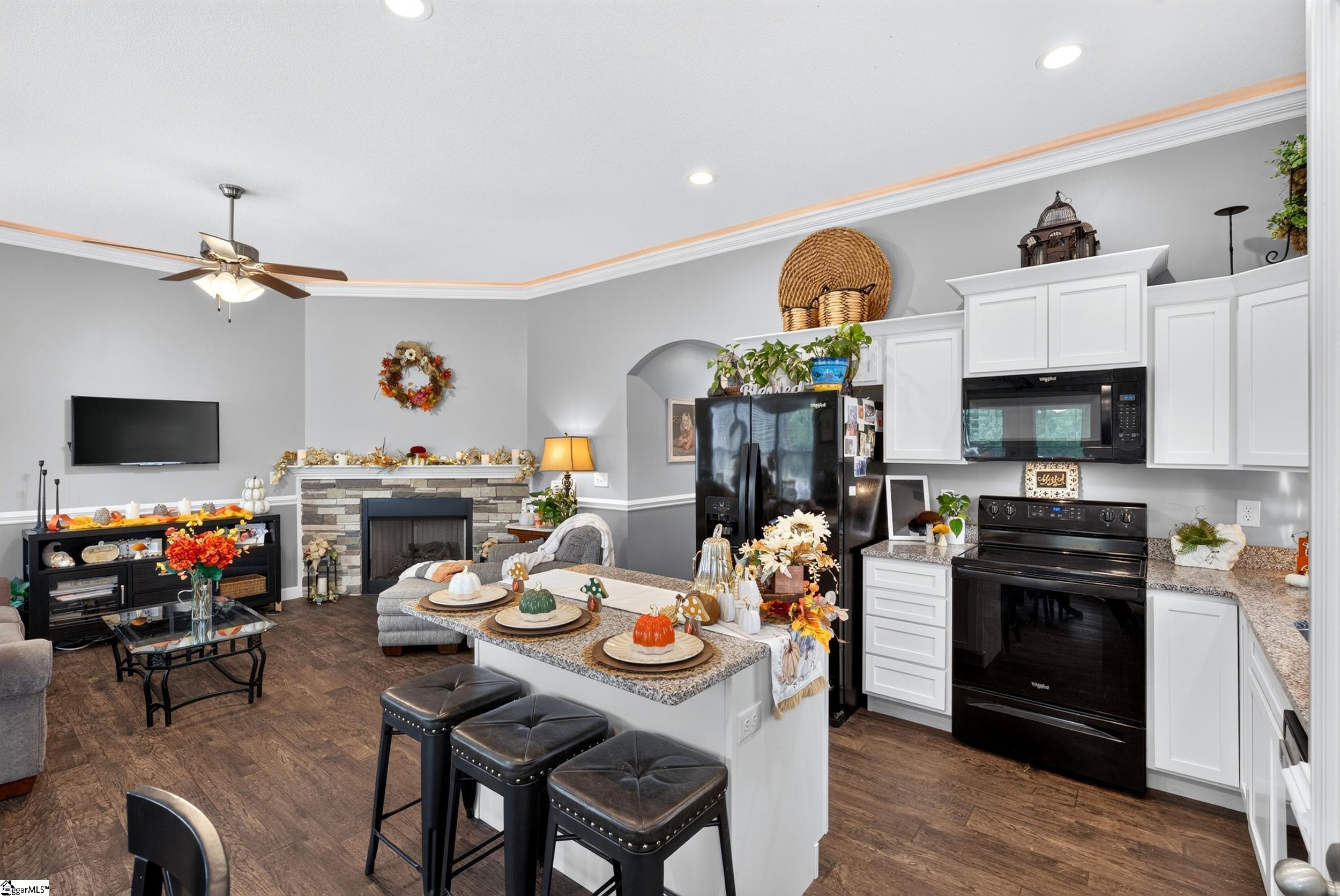 Open kitchen and living room with a granite island, black appliances, and stone fireplace.