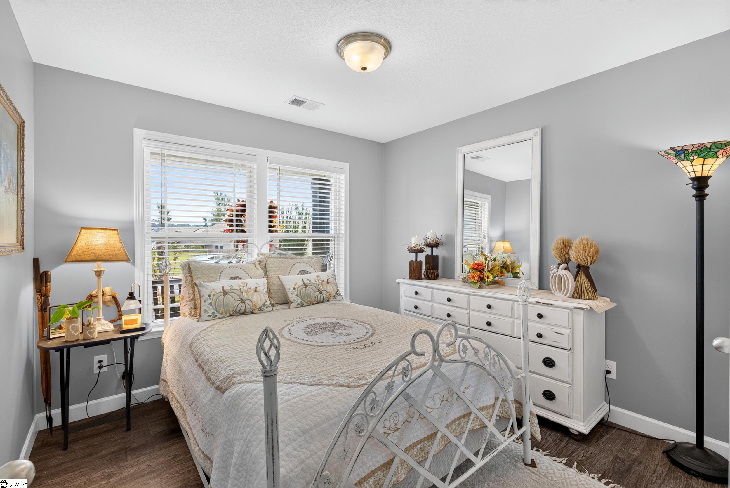 Bedroom with a white metal bed, cream pumpkin-patterned bedding, two windows, and a white dresser with mirror.