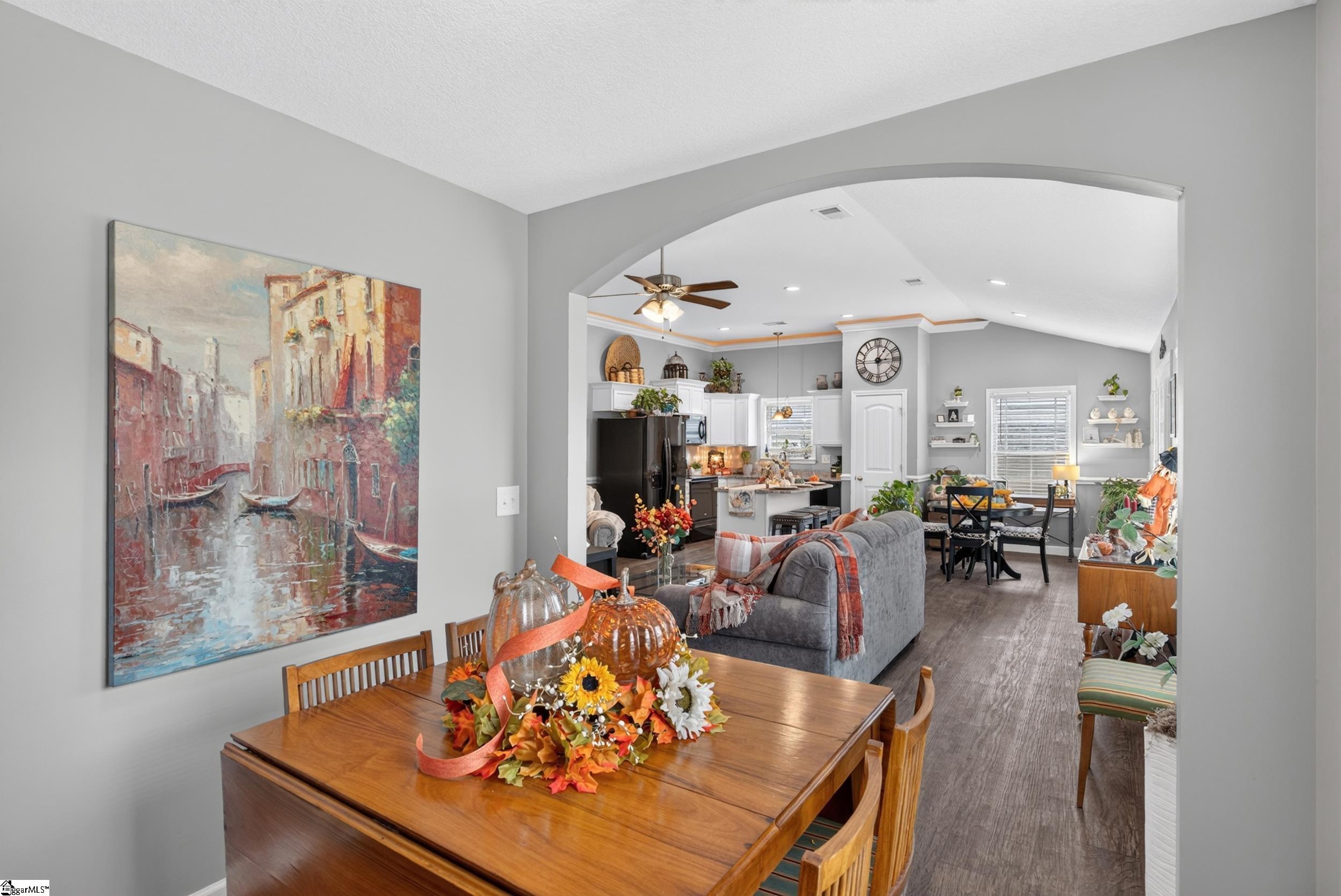 Open-plan dining and living room with a wooden table, arched opening, and kitchen beyond.