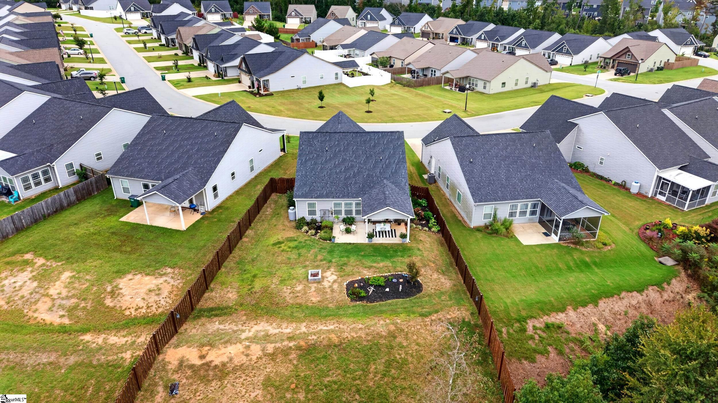 Aerial view of a gray house and fenced backyard with a covered patio and garden beds.