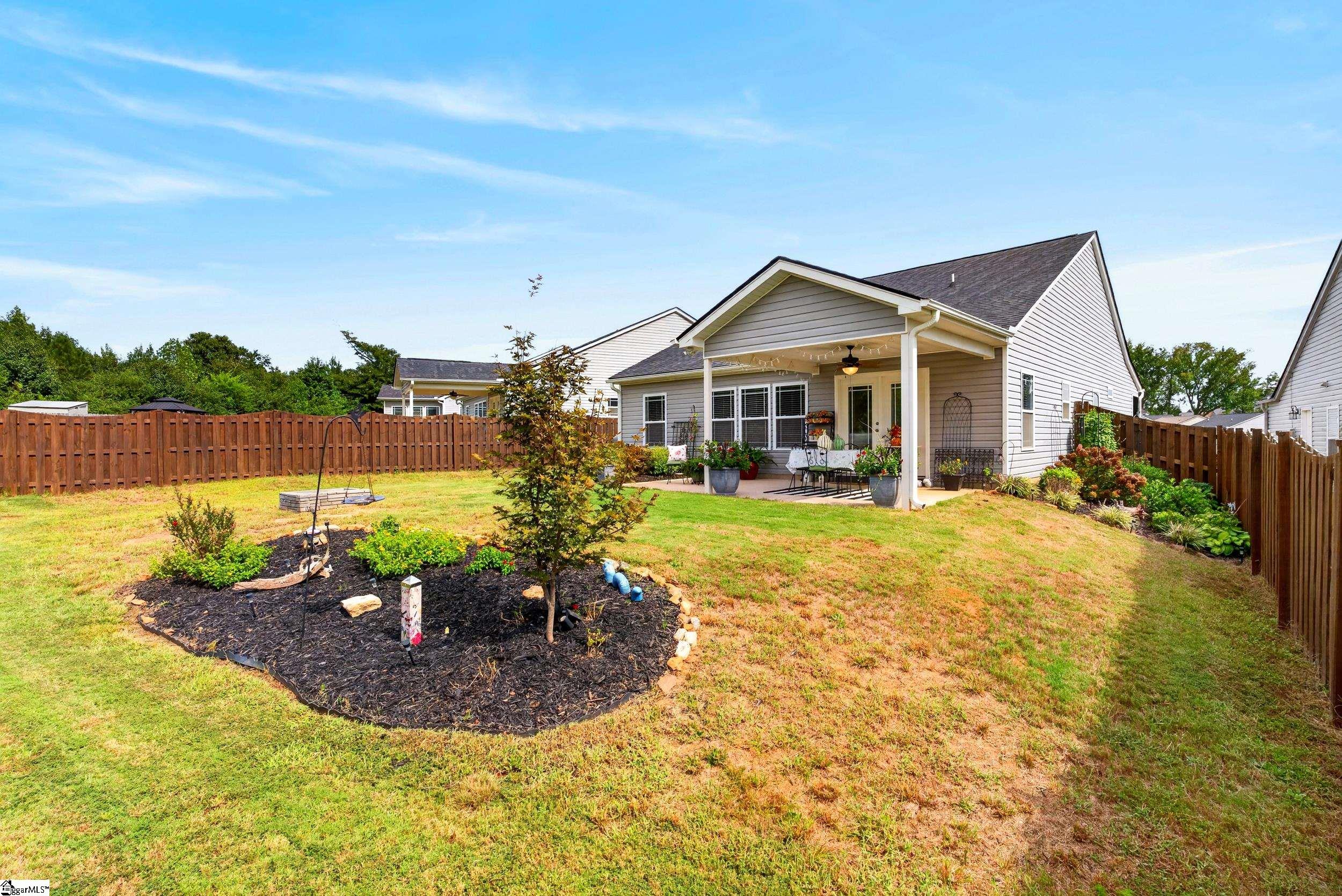 Home’s rear patio and fenced backyard with outdoor dining furniture and a landscaped garden bed.