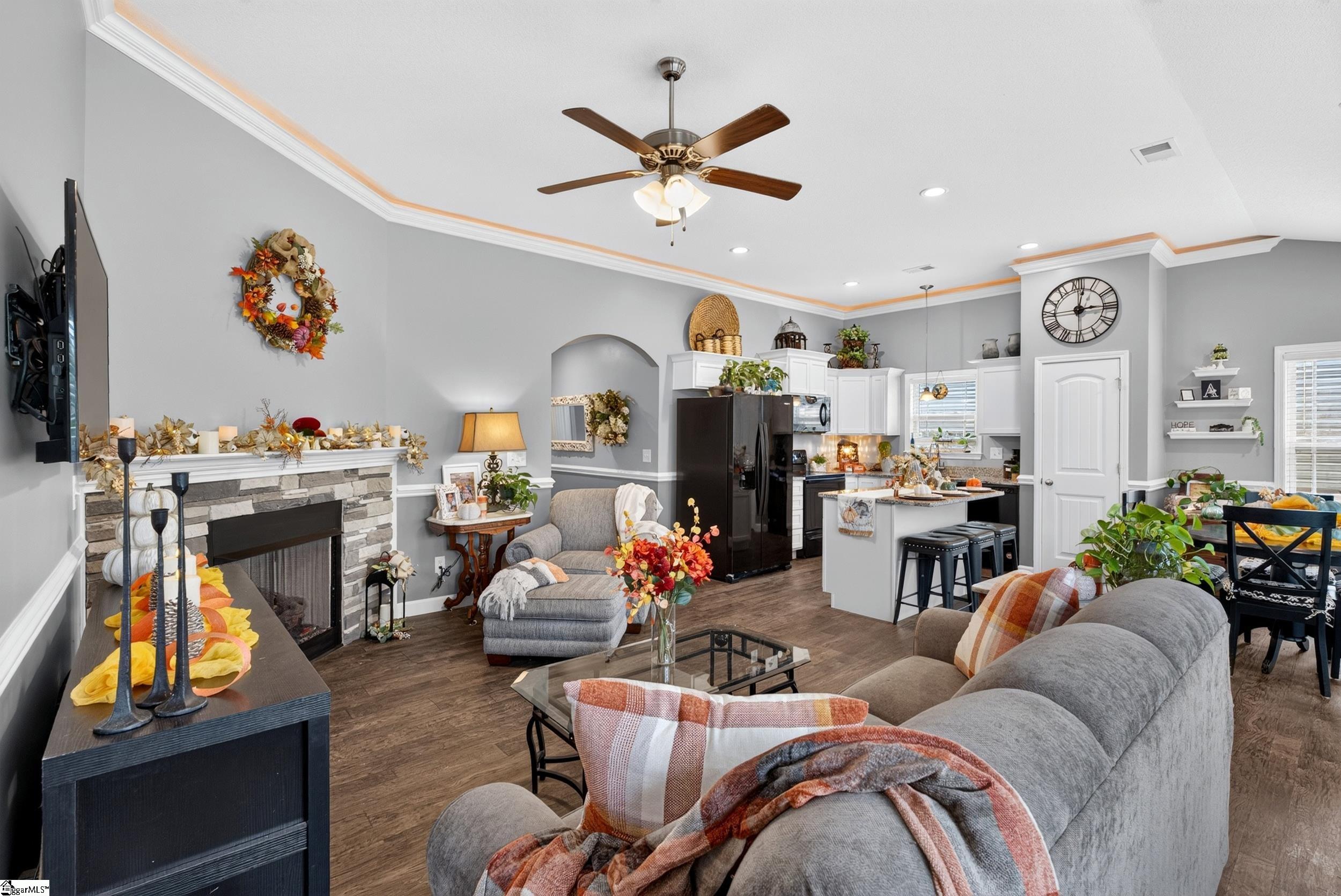 Open-plan living room and kitchen with a stone fireplace, gray seating, and white cabinets.