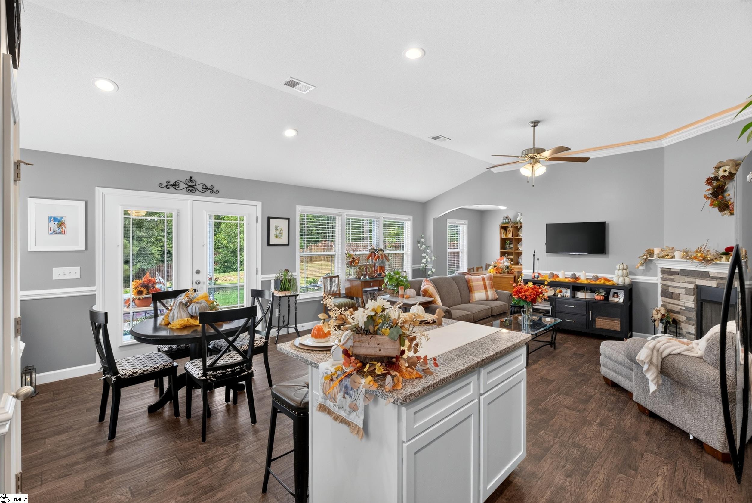 Open kitchen and living room with granite island, dining table, sofa, and stone fireplace.
