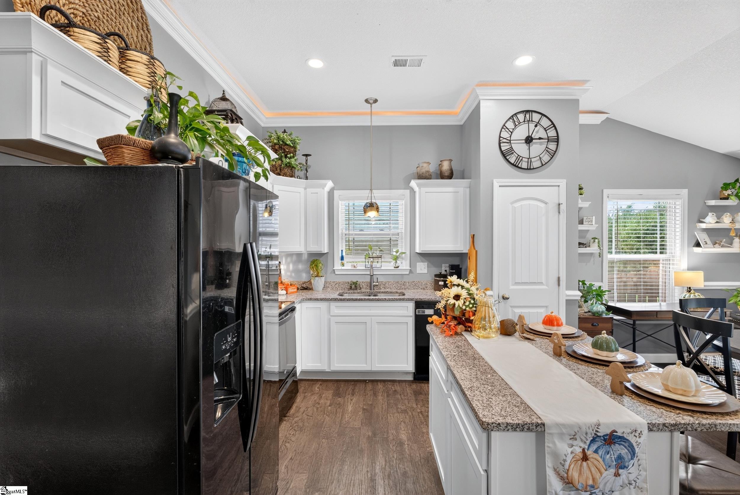 Kitchen with white cabinets, granite island, black refrigerator, and adjoining dining area.