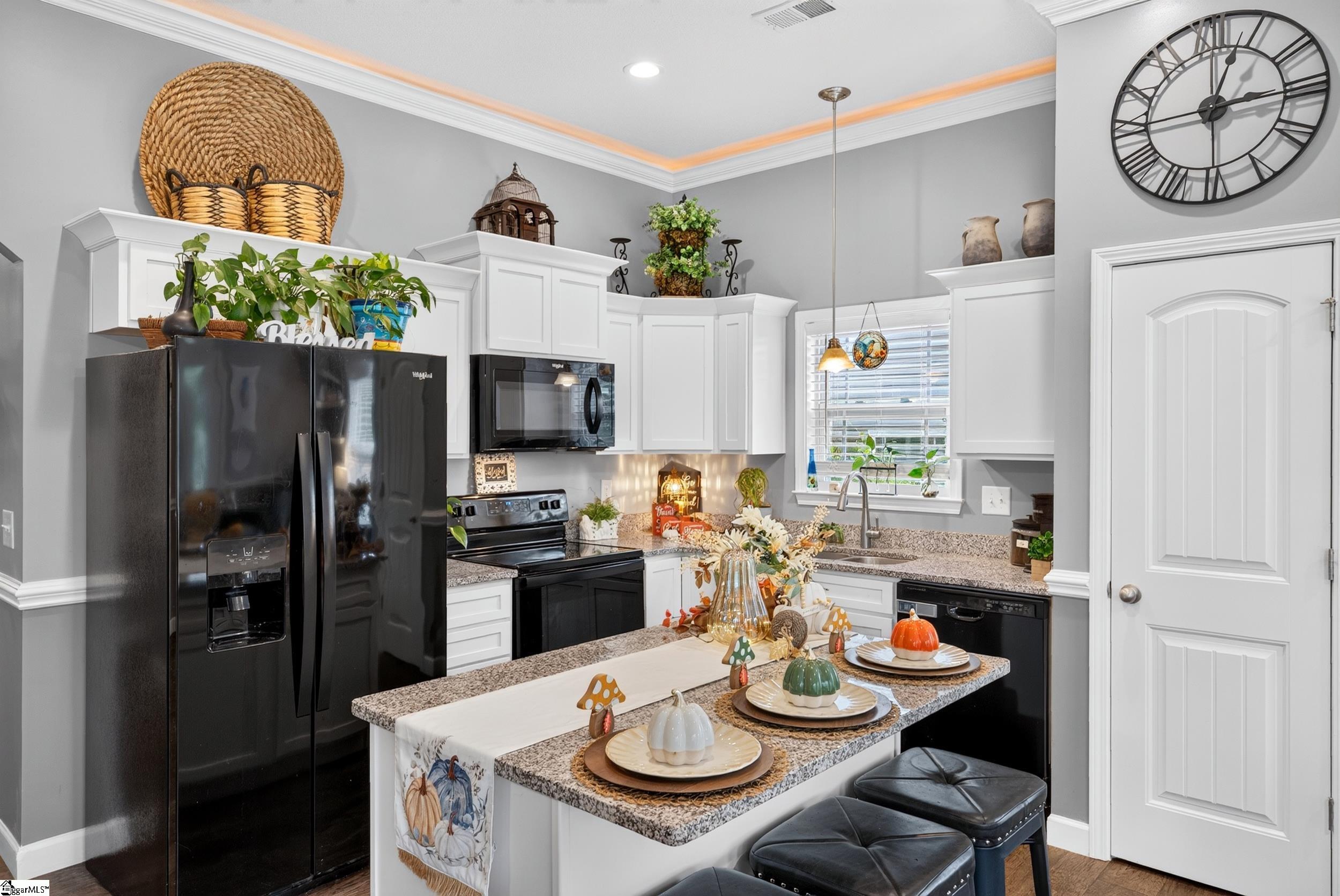 Kitchen with white cabinets, black appliances, and a granite island decorated with autumn pumpkins.