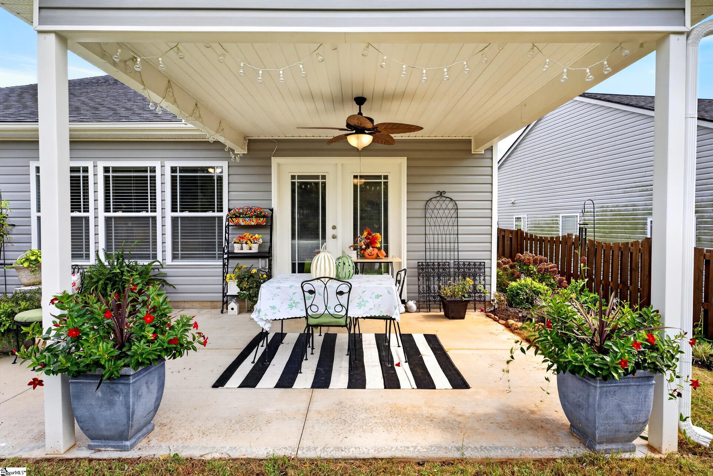 Covered patio with dining table, striped rug, string lights, and colorful potted flowers