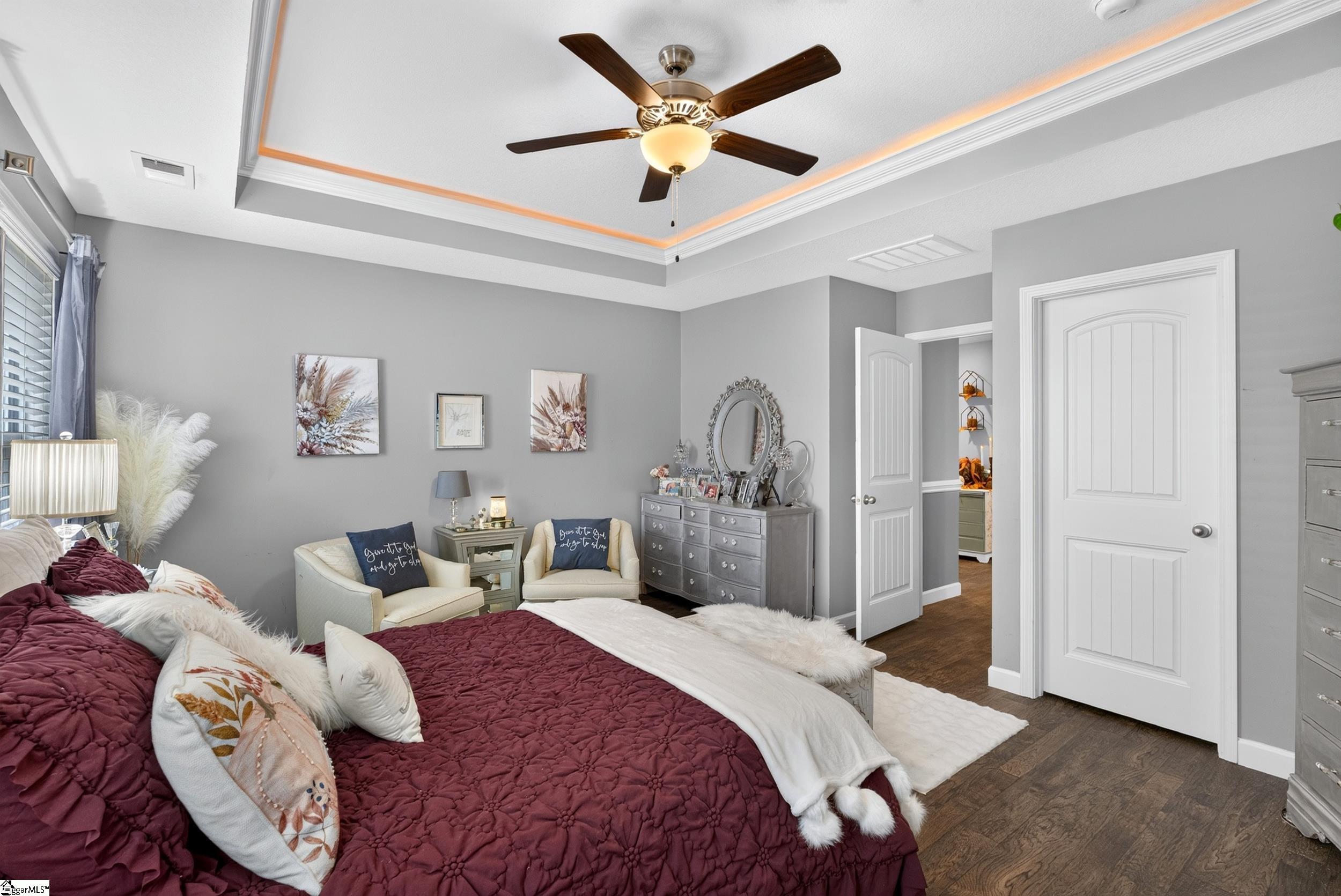 Furnished bedroom with a burgundy quilted bed, tray ceiling, sitting area, and silver dresser.
