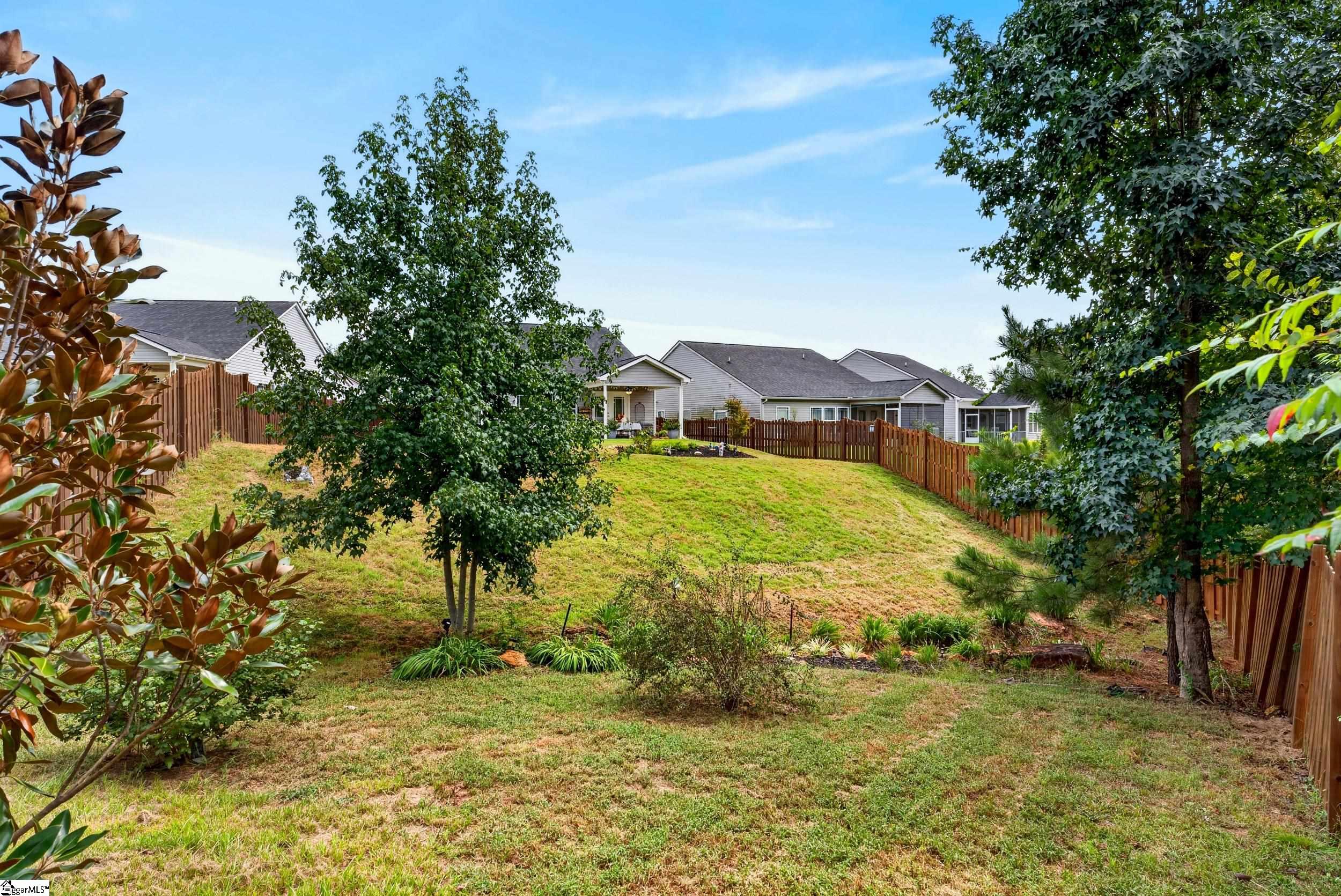 Sloping backyard with mature trees, a wooden fence, and neighboring homes beyond.
