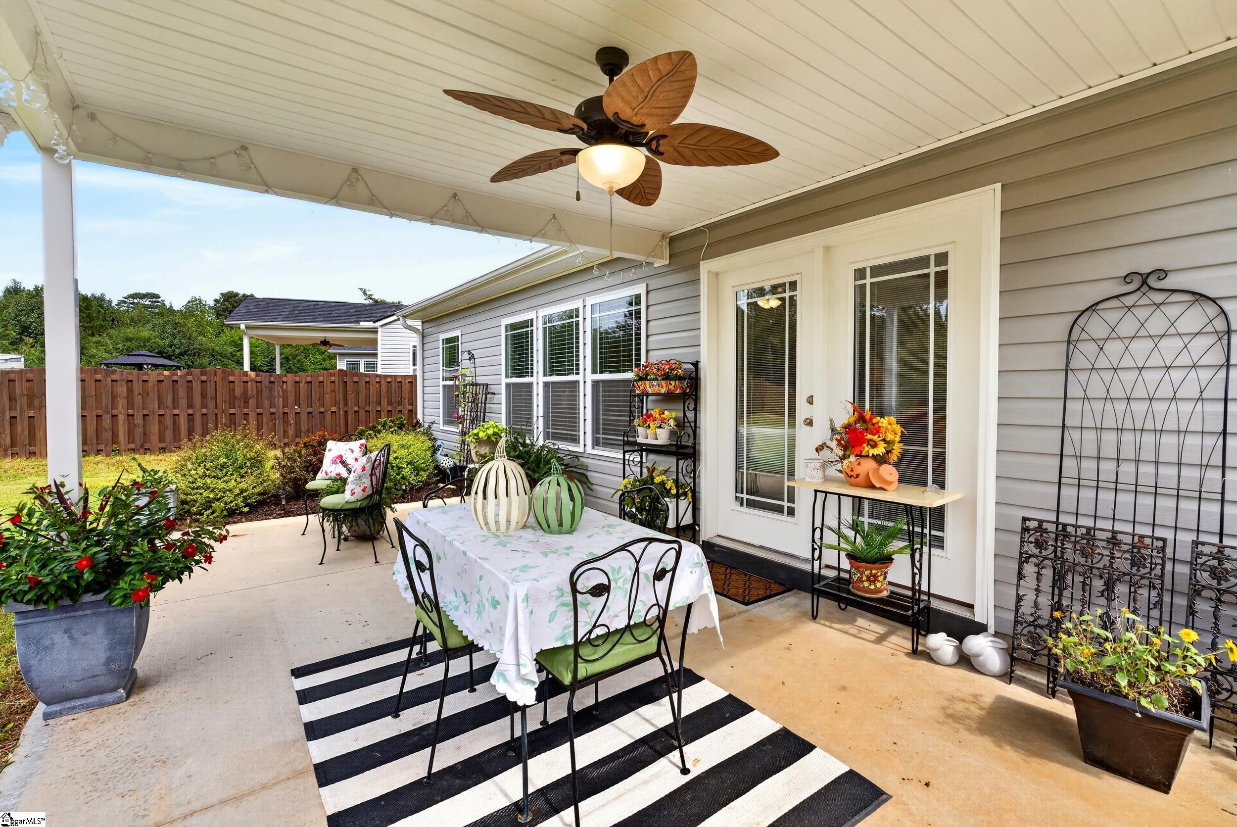 Covered patio with outdoor dining set, ceiling fan, potted flowers, and fenced yard.