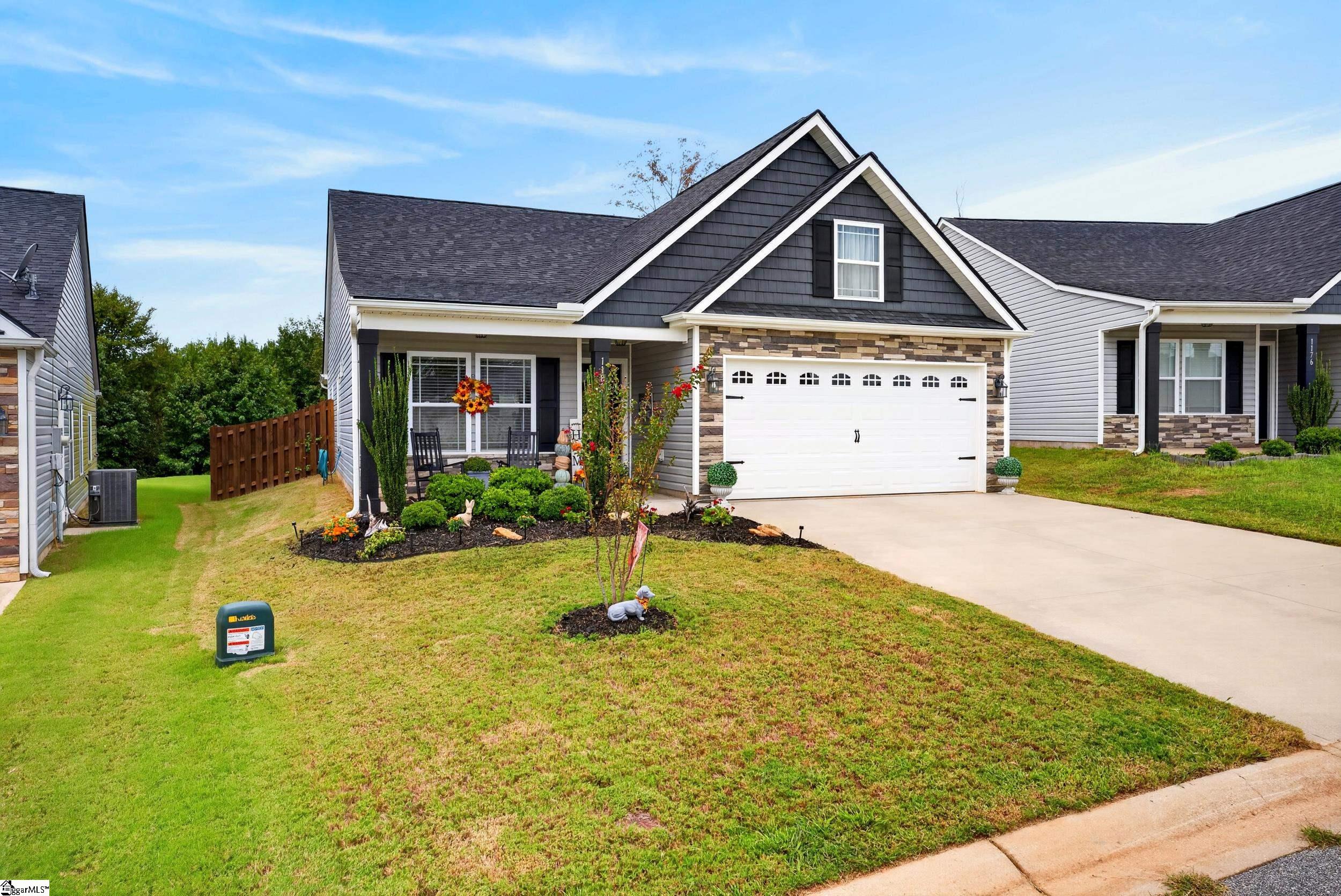 Gray two-story home with stone accents, white double garage, landscaped flower beds, and front lawn.