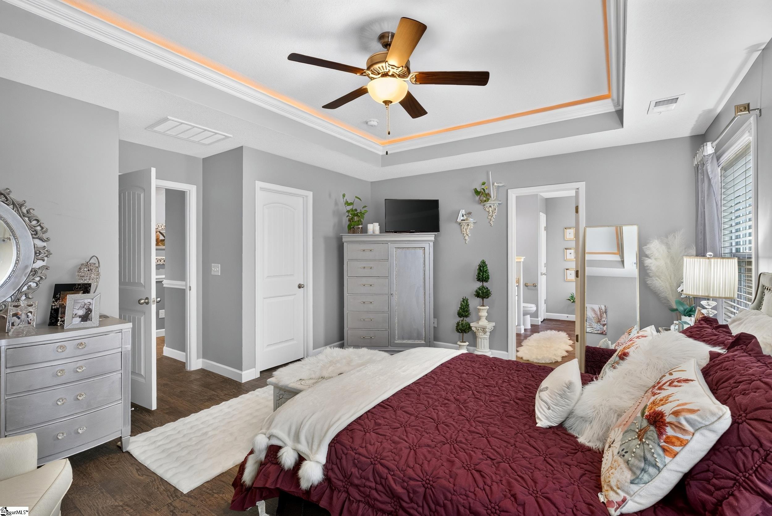 Furnished bedroom with a burgundy quilted bed and a tray ceiling with warm accent lighting.