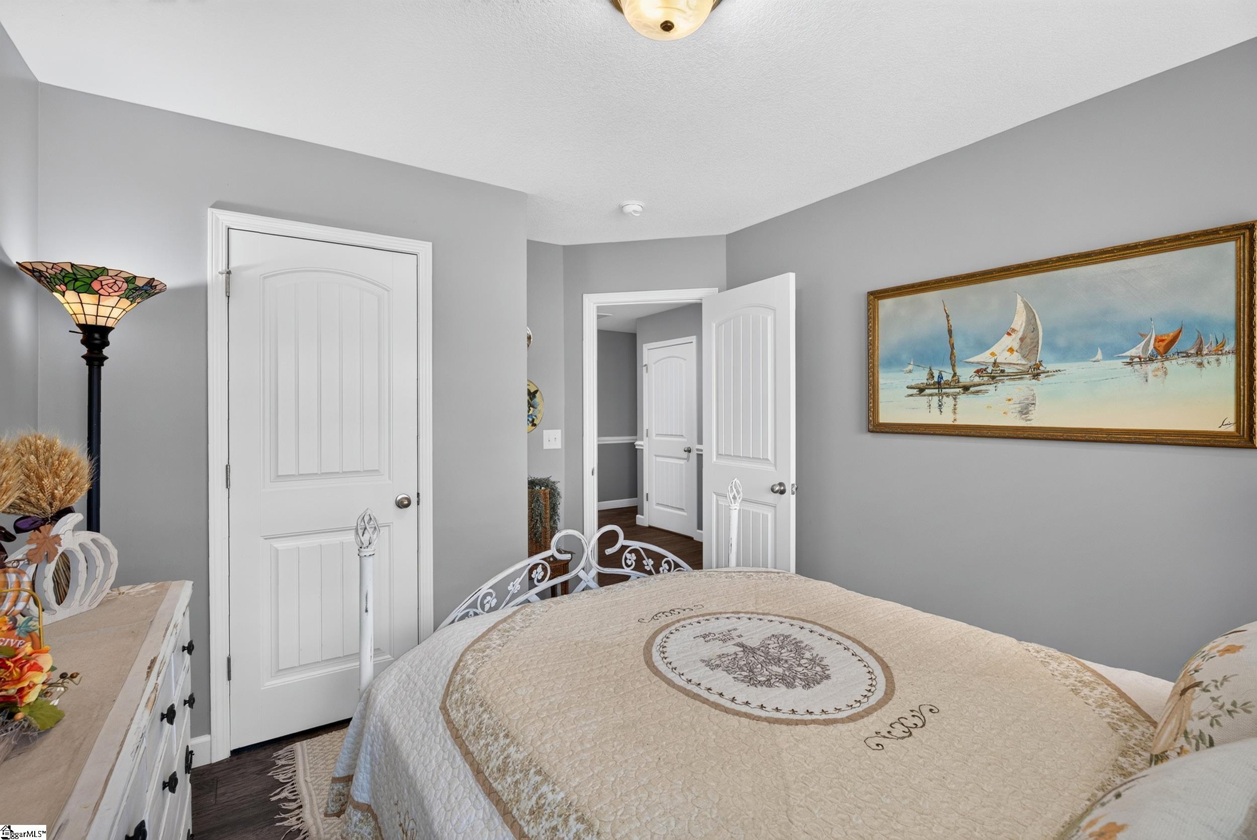 Bedroom with a cream quilted bed, gray walls, and framed sailboat painting.