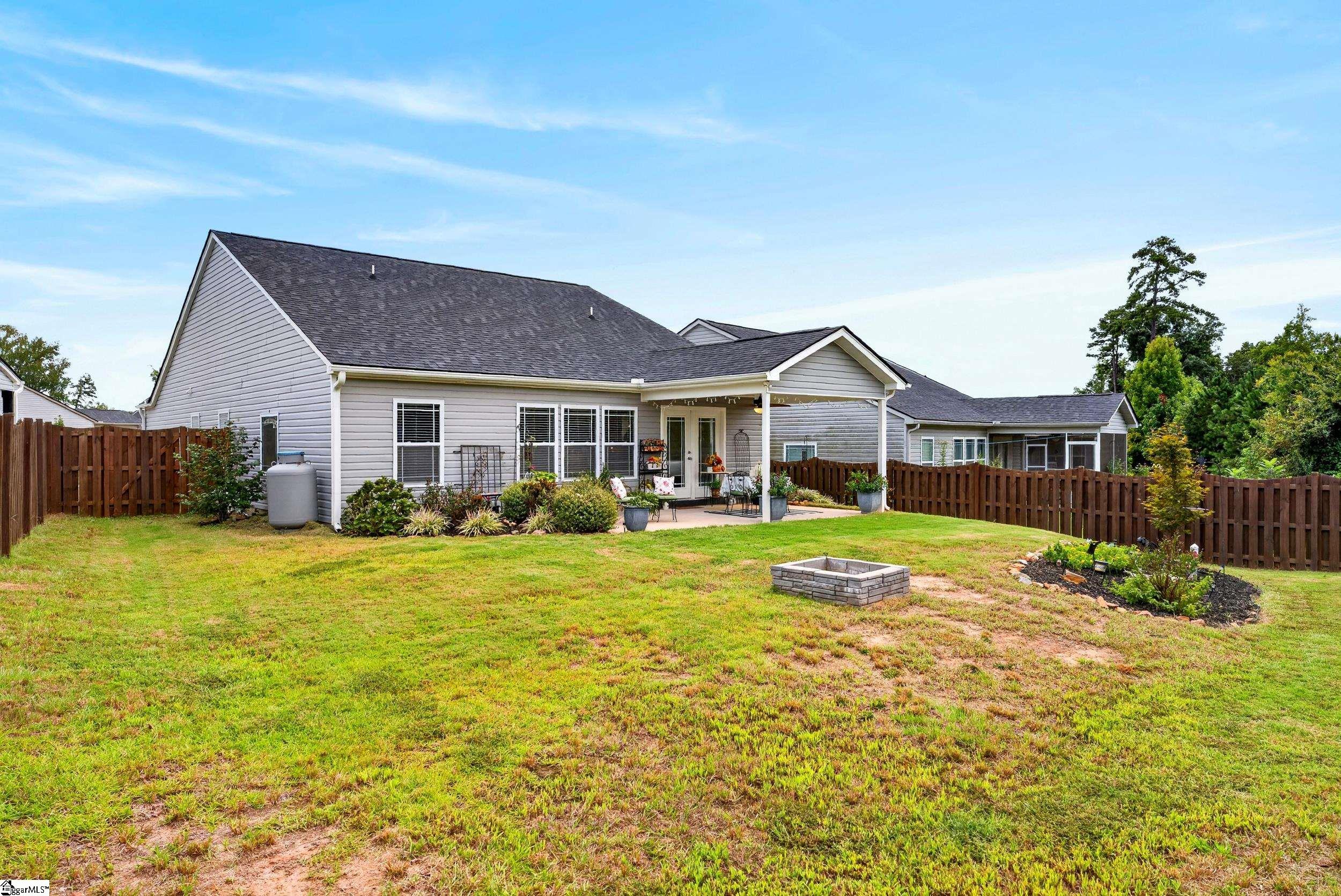 Gray home with a covered patio overlooking a fenced backyard and stone fire pit.