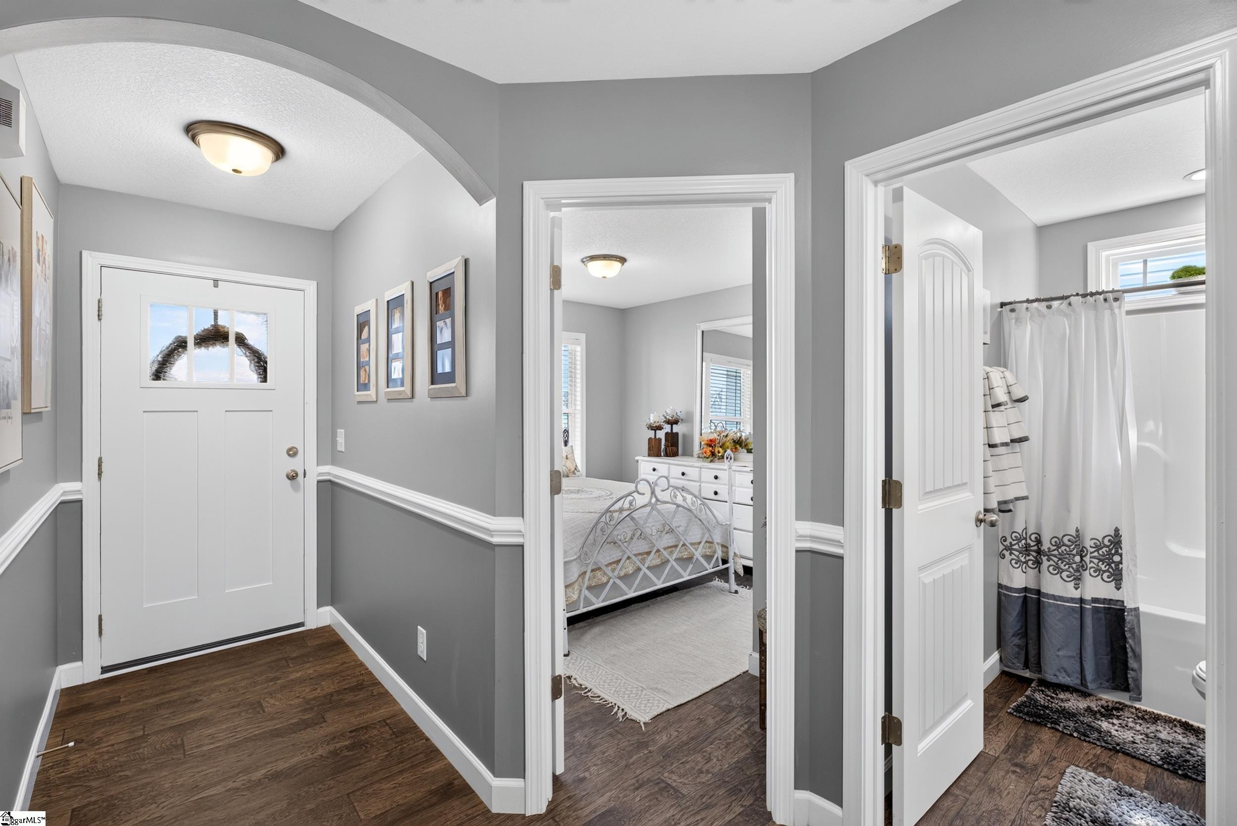 Gray entry hallway with dark wood floors, opening onto a furnished bedroom and bathroom.